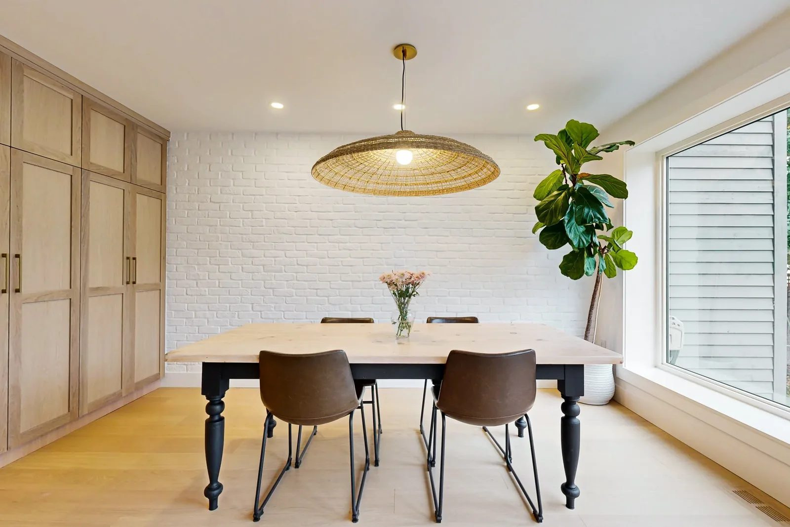 Bright dining room renovation with white brick, oak cabinetry, a woven pendant, and a large window.