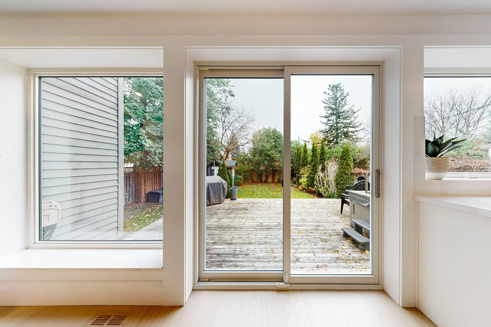 Bright finished room with warm white trim, light oak floors, and a sliding door opening to a backyard deck.