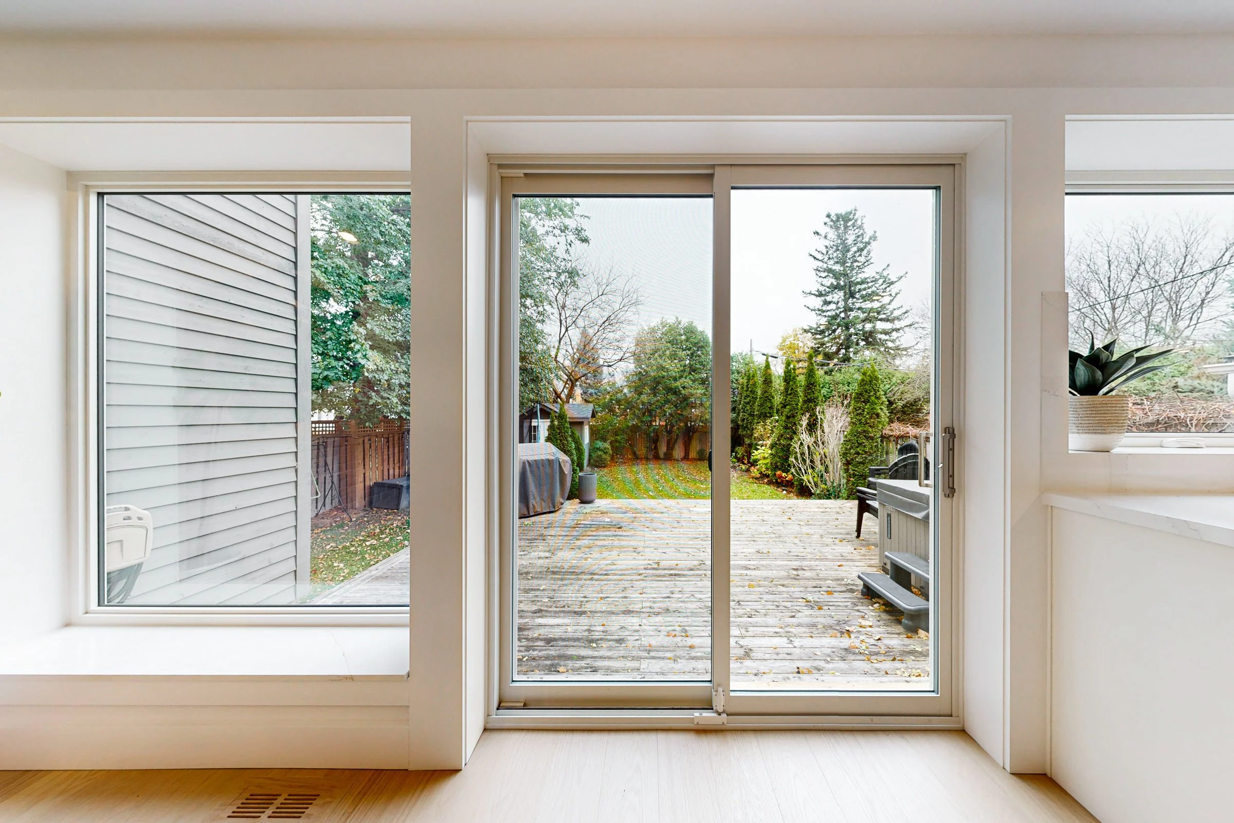 Bright finished room with warm white trim, light oak floors, and a sliding door opening to a backyard deck.
