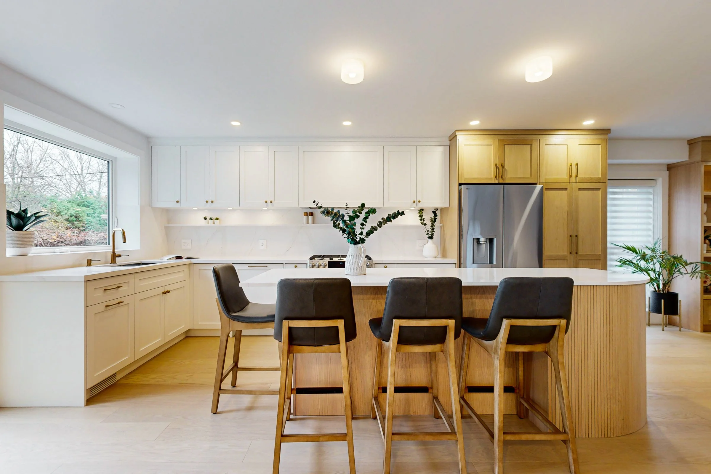 Bright open kitchen with white cabinetry, oak island seating and brass accents in a finished renovation.