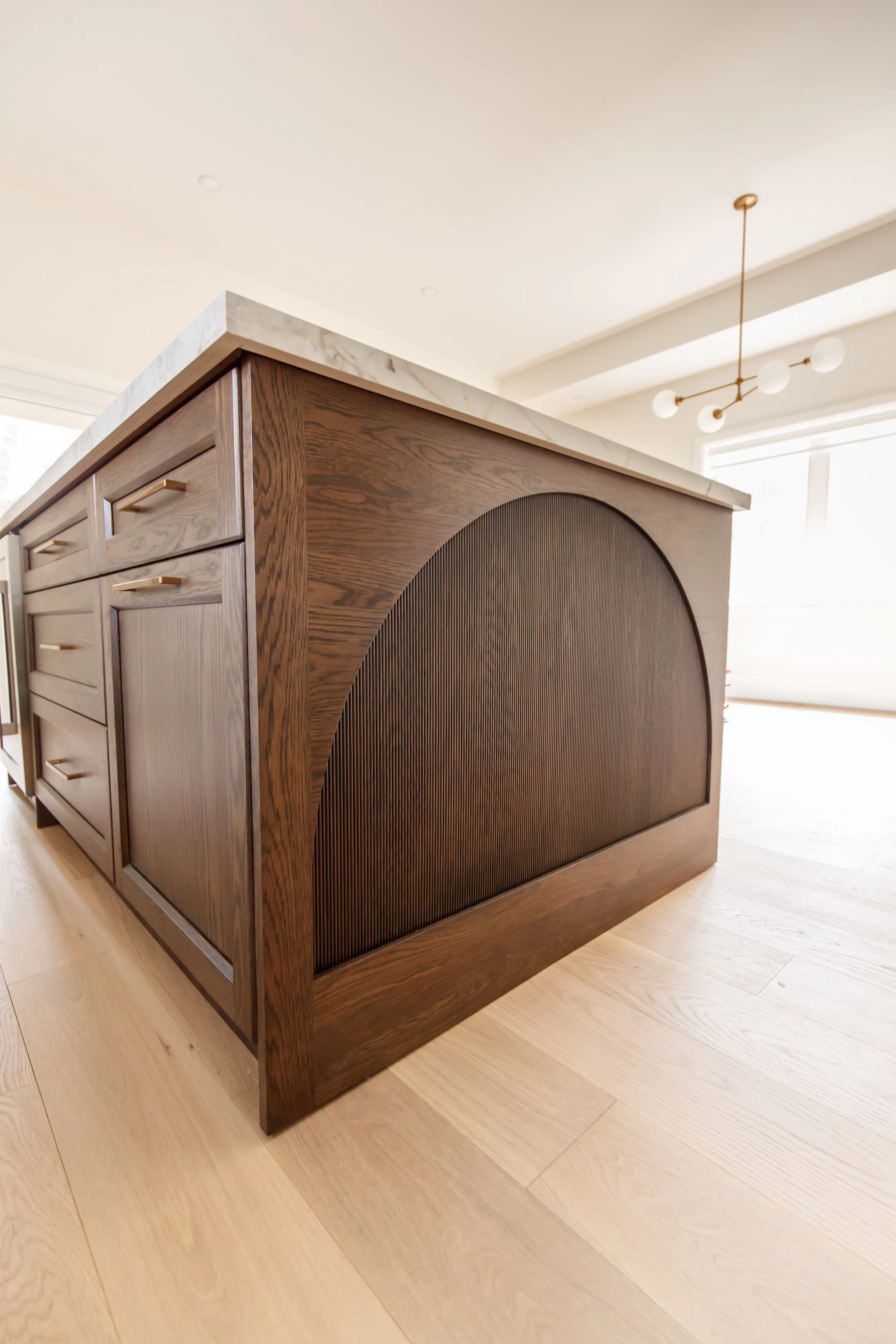 Close detail of a walnut island end panel with reeded arch and marble waterfall edge.