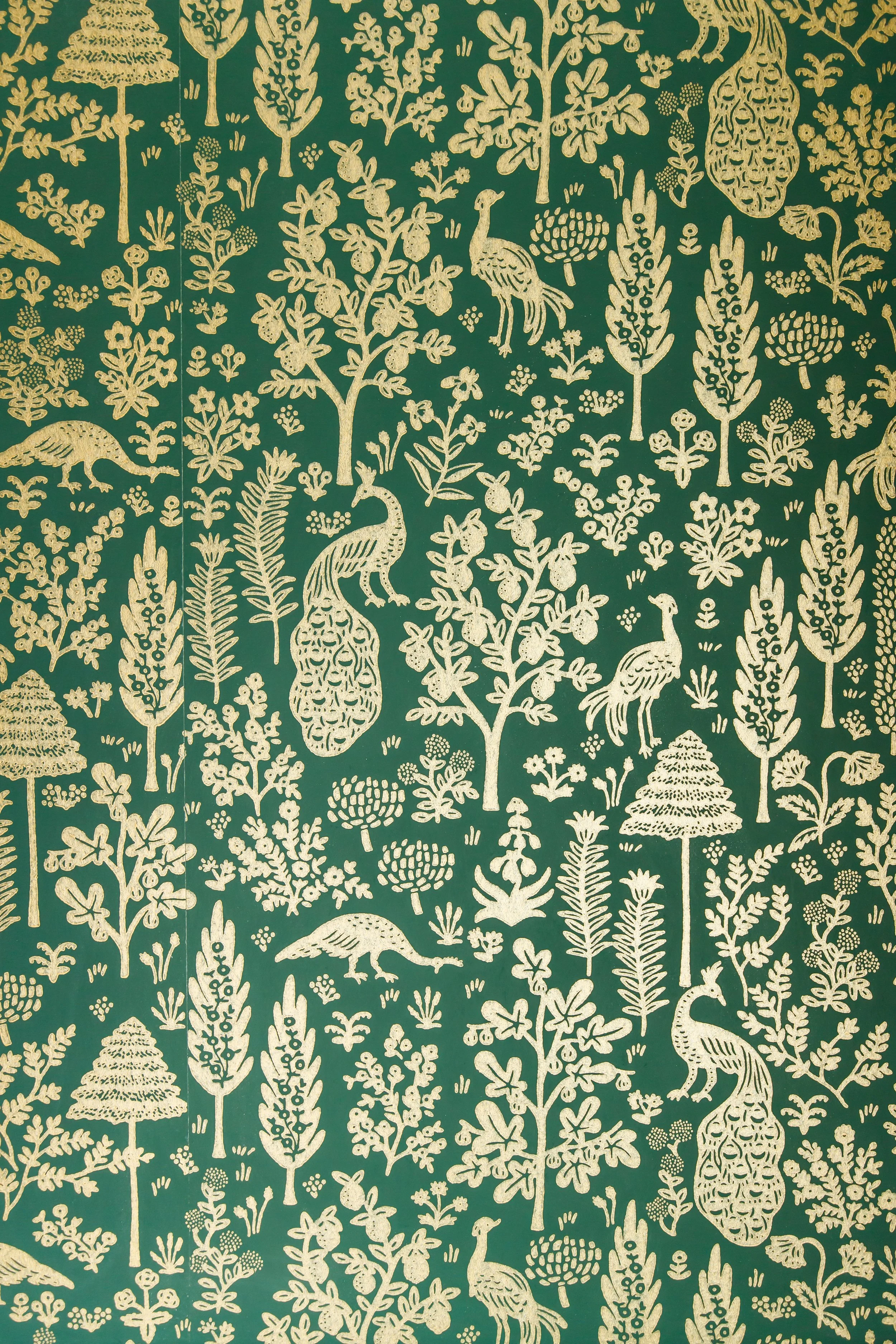 Detail of green and gold botanical wallpaper with peacocks and stylised trees.