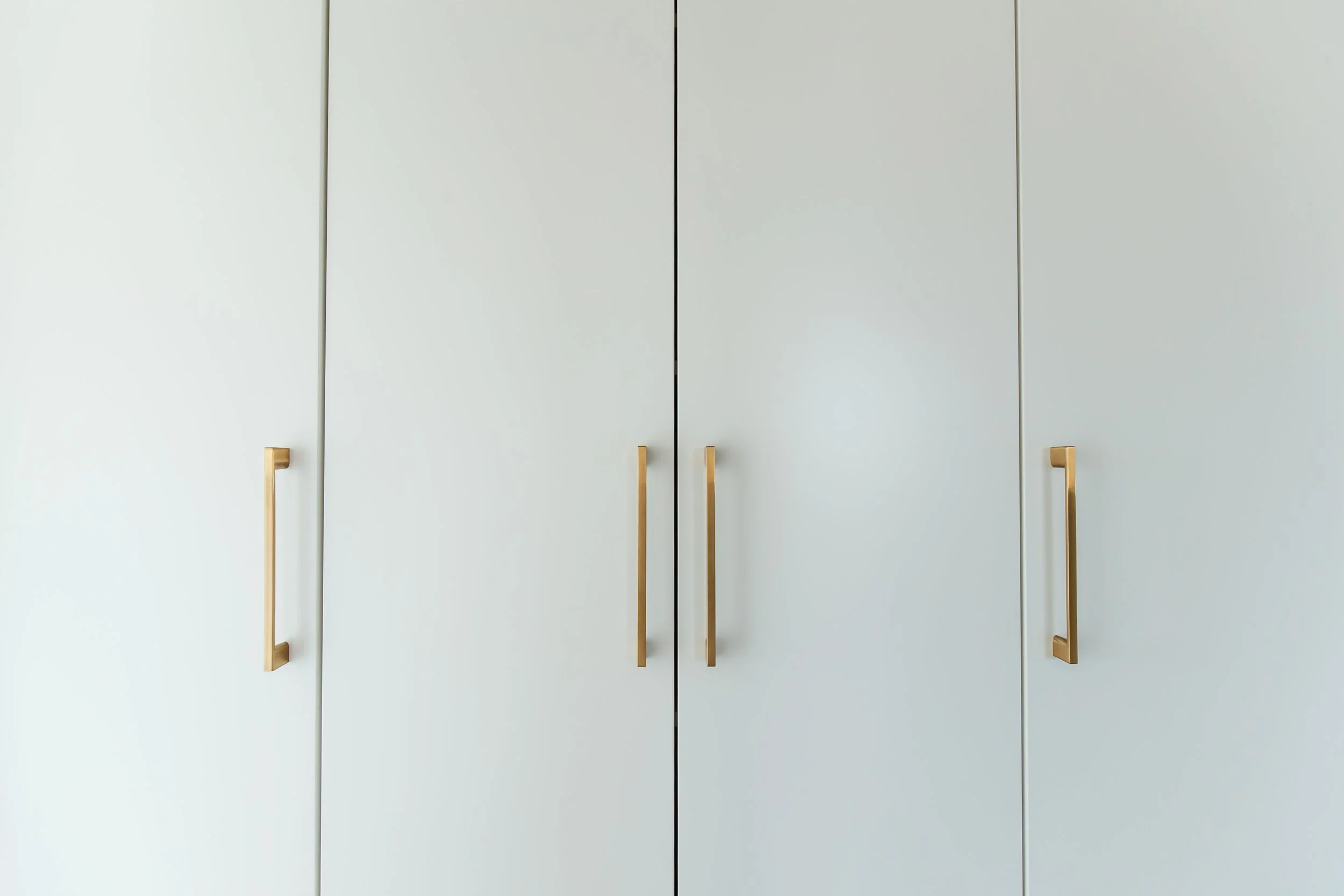 Close view of built-in closet slab doors with long polished brass bar pulls.