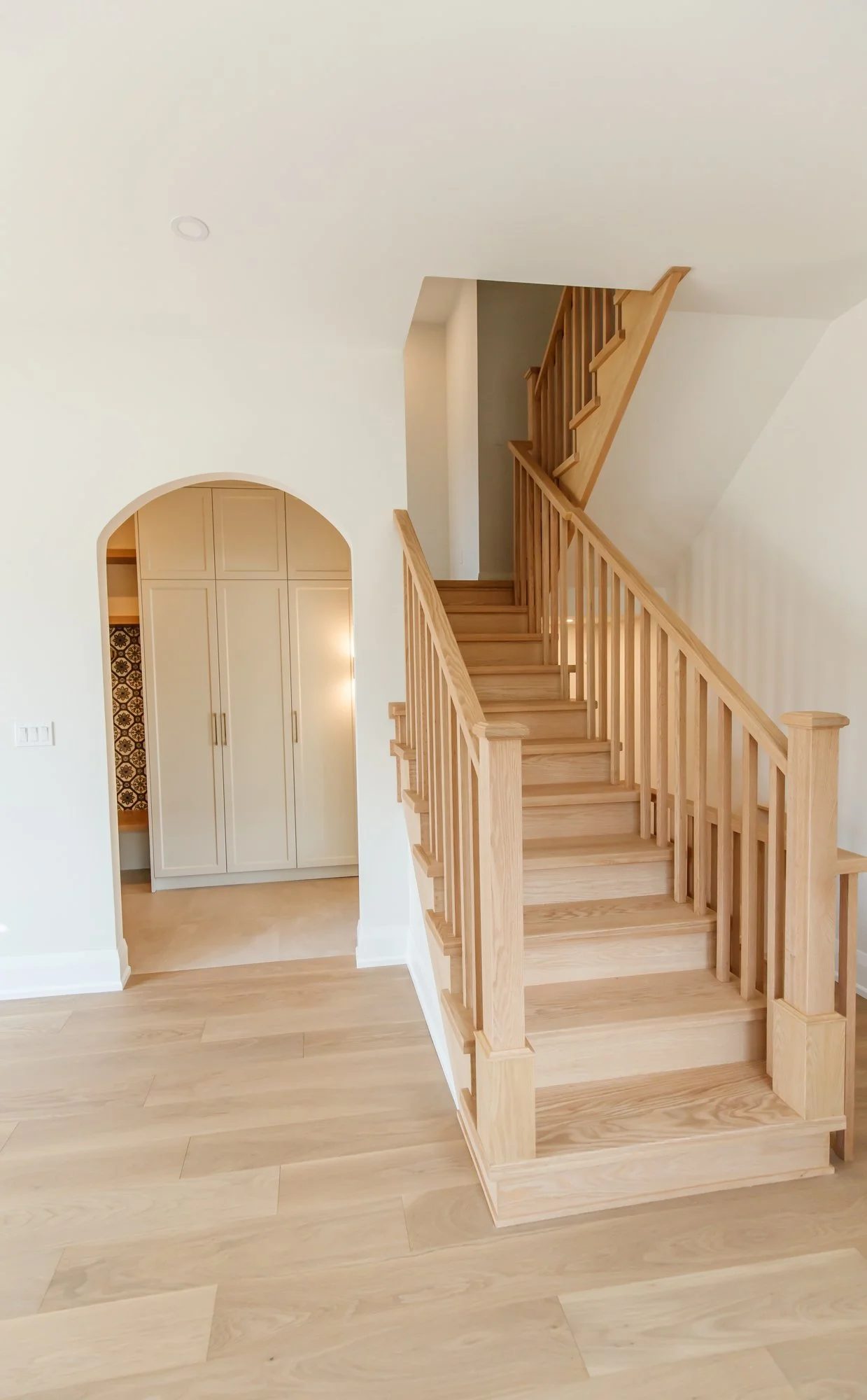 Finished hallway with natural oak stairs, warm white walls, and an arched opening to a kitchen.