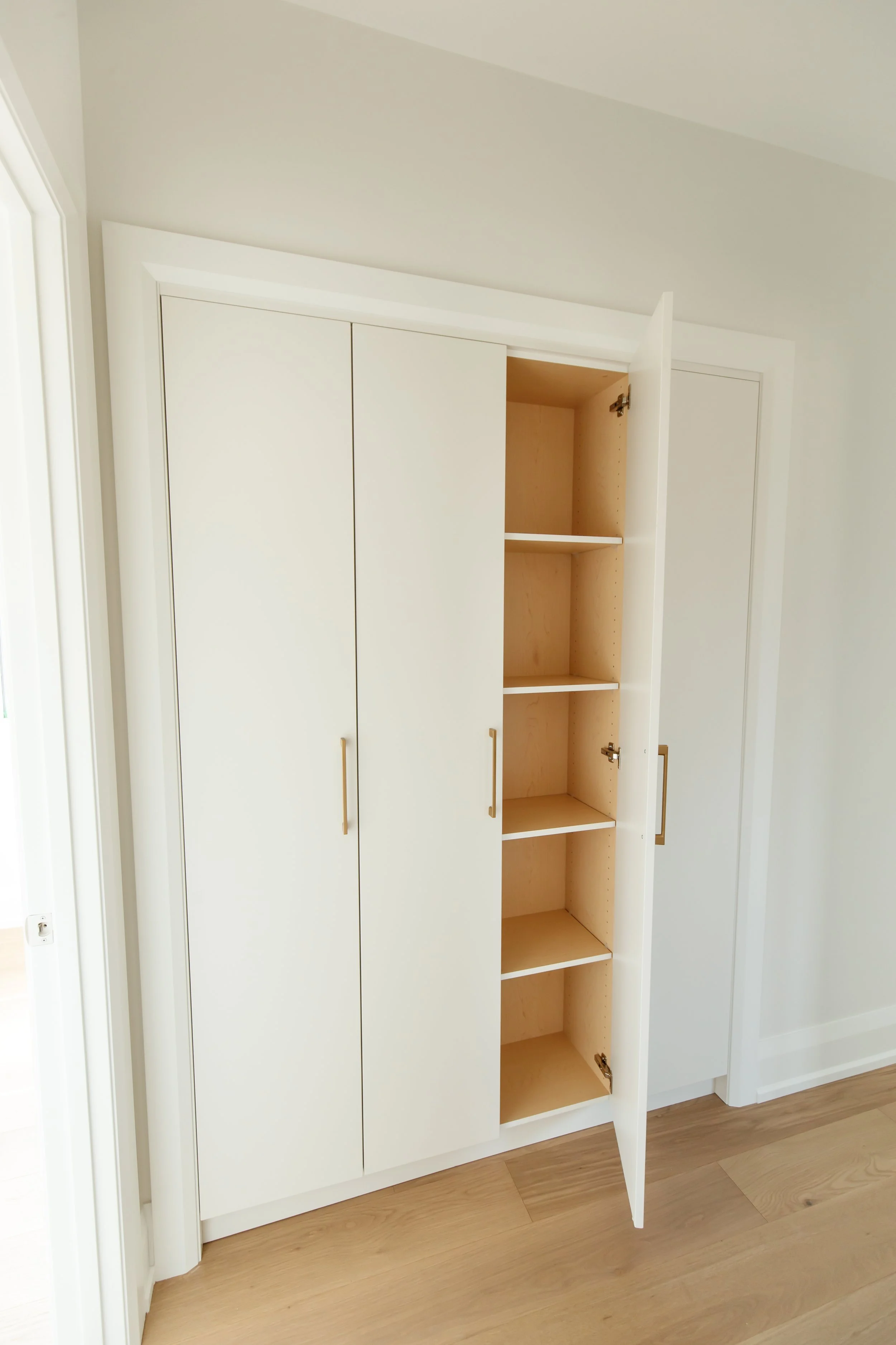 Built-in linen closet with open door revealing birch plywood interior and adjustable shelves.