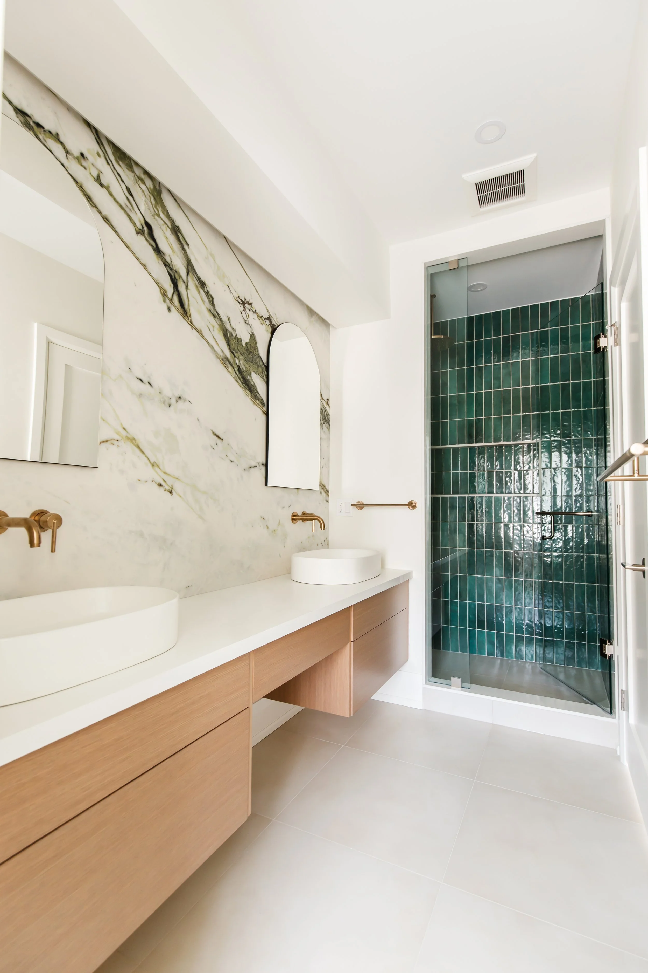 Primary bath with marble vanity wall and emerald tile shower behind clear glass.