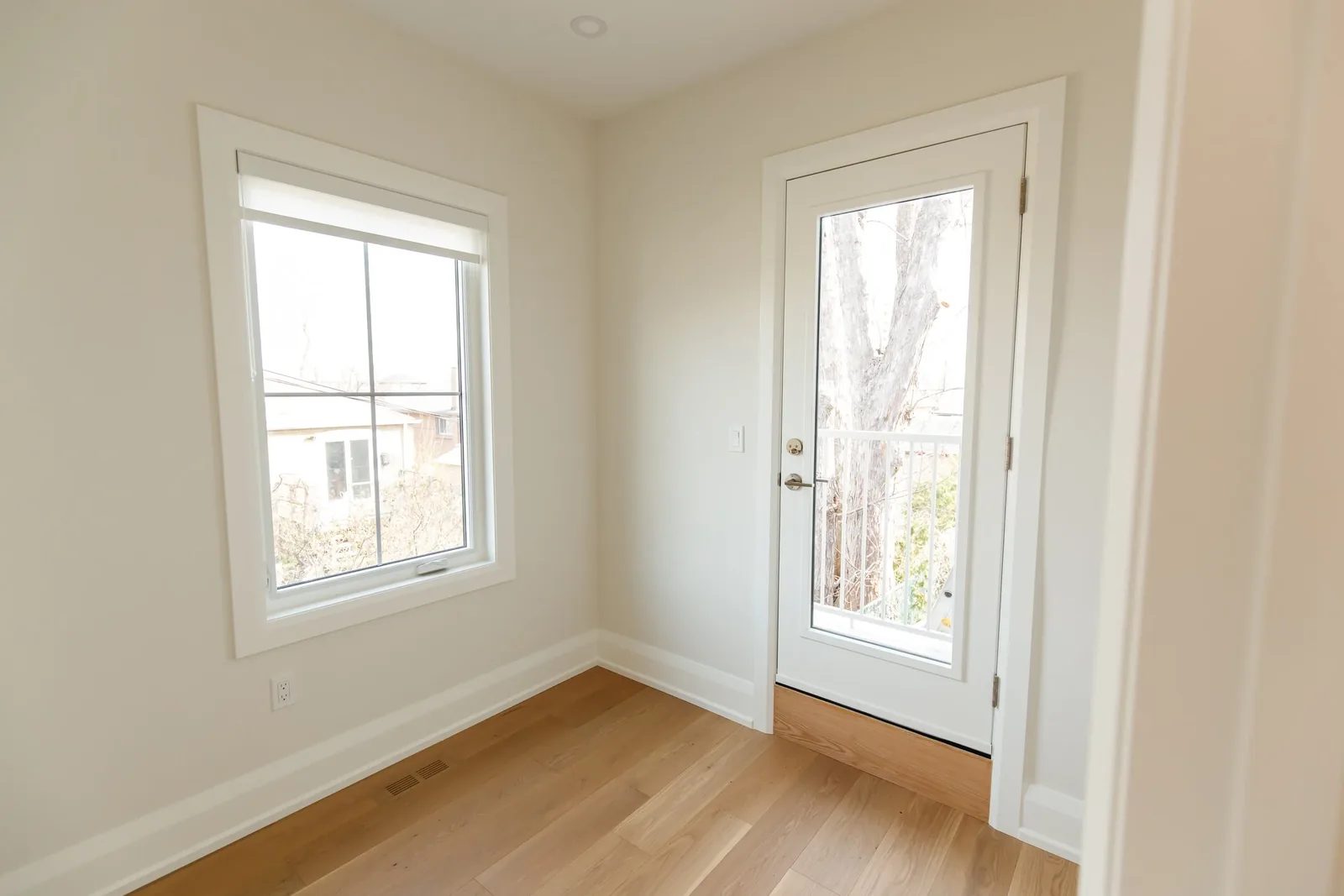 Empty bedroom with square casement window and glass exterior door overlooking bare trees.