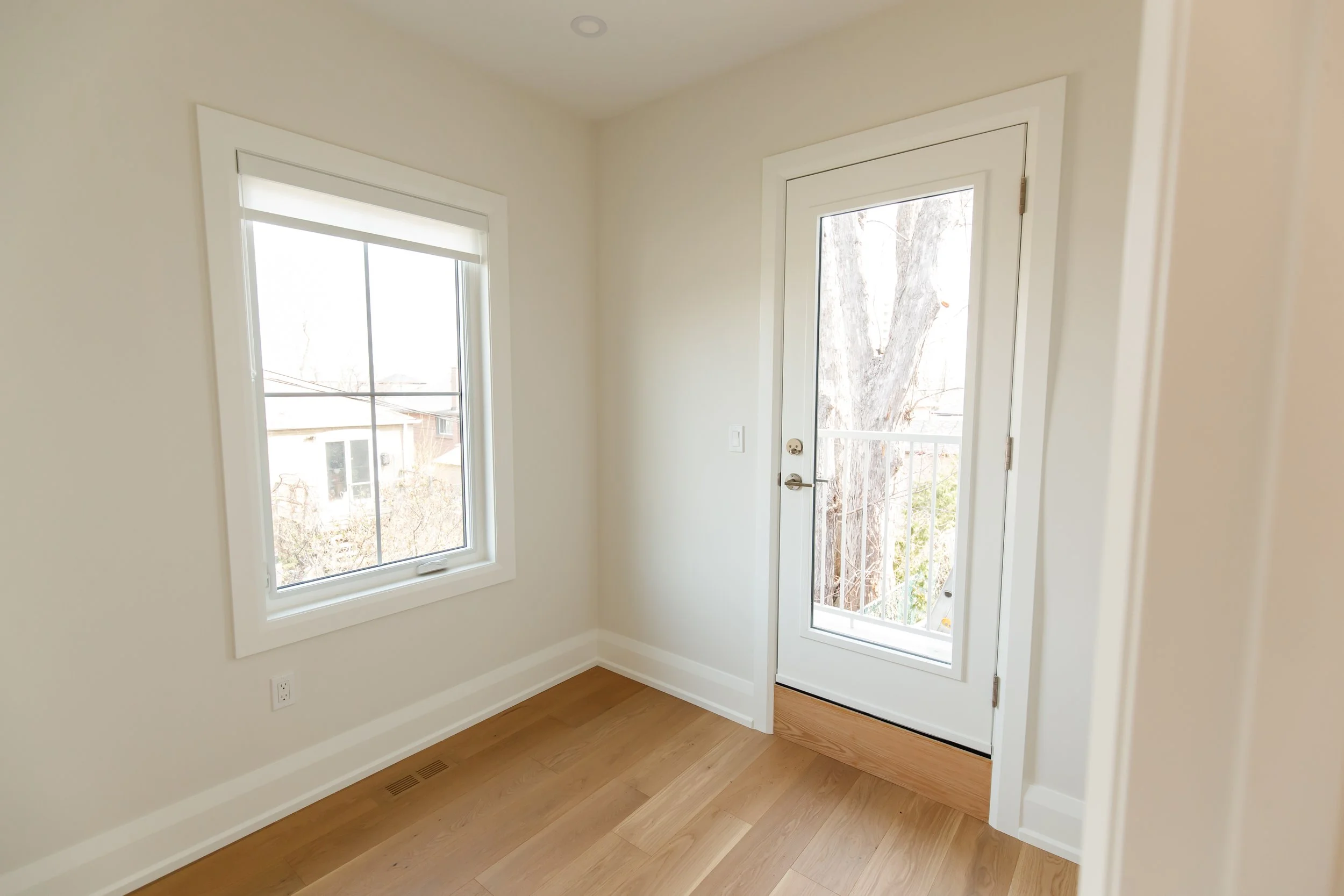 Empty bedroom with square casement window and glass exterior door overlooking bare trees.