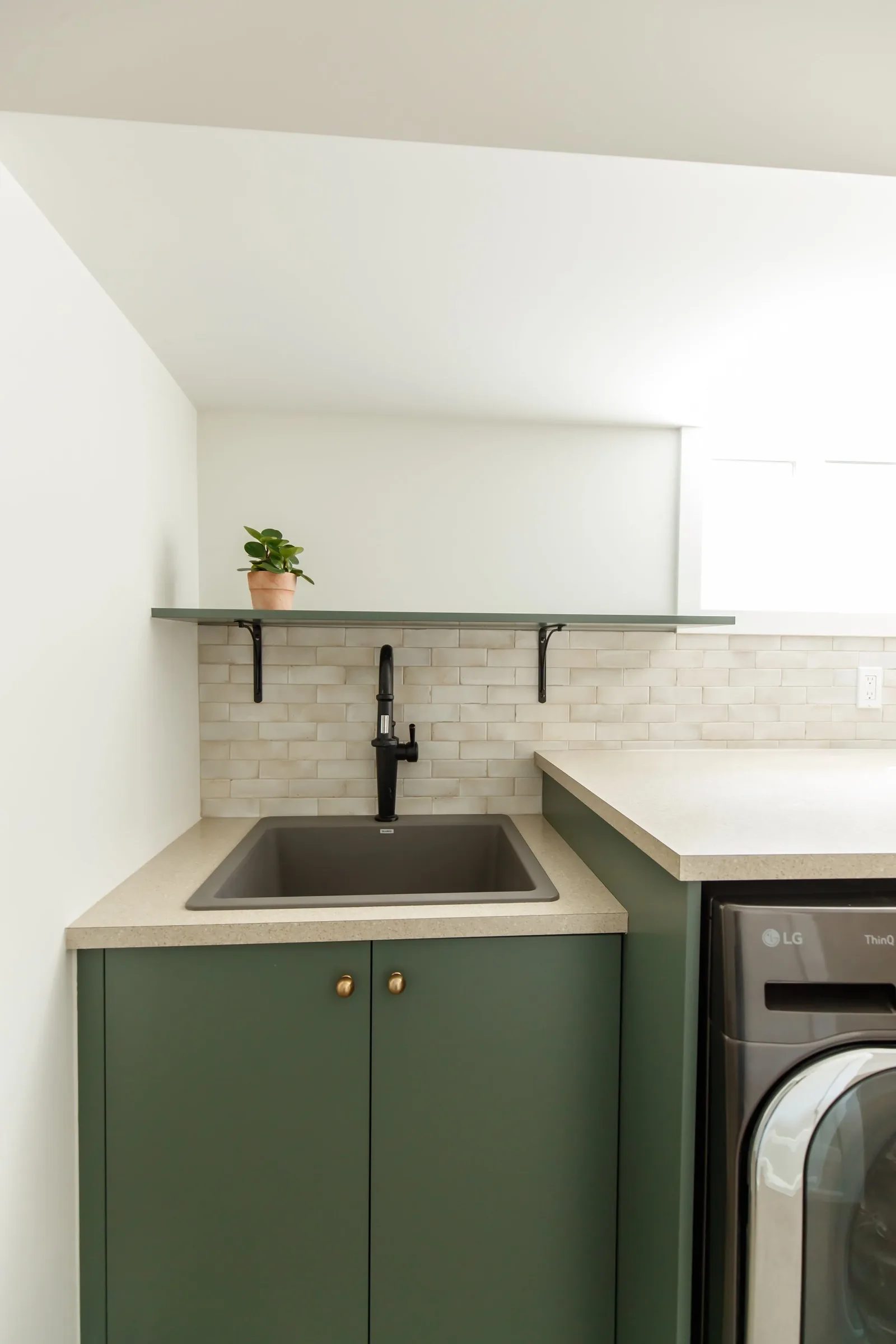 Laundry detail showing dark green cabinets, a graphite utility sink, and a handmade zellige backsplash.