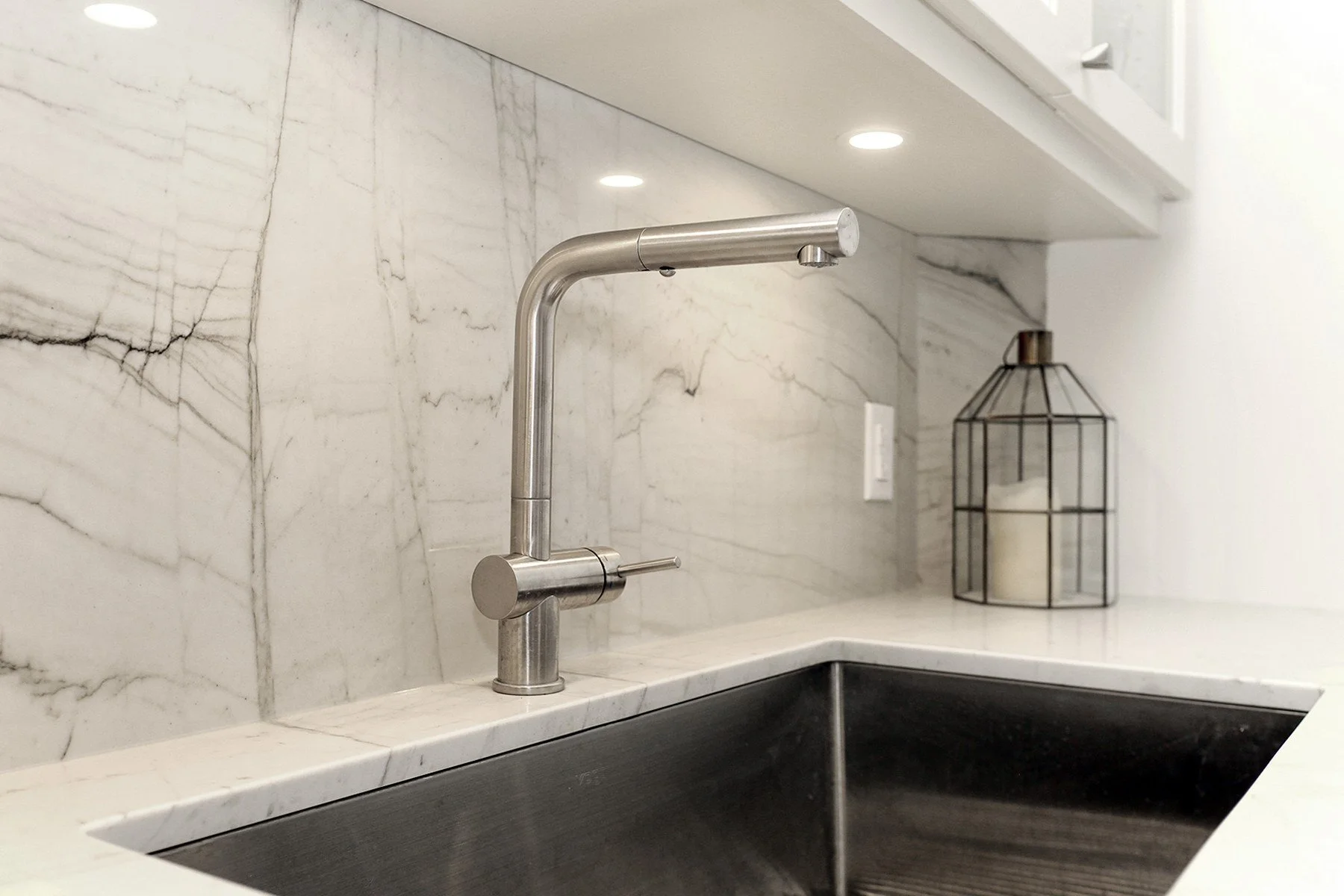 Contemporary kitchen detail featuring a sleek stainless steel faucet, undermount sink, and stunning white marble backsplash.