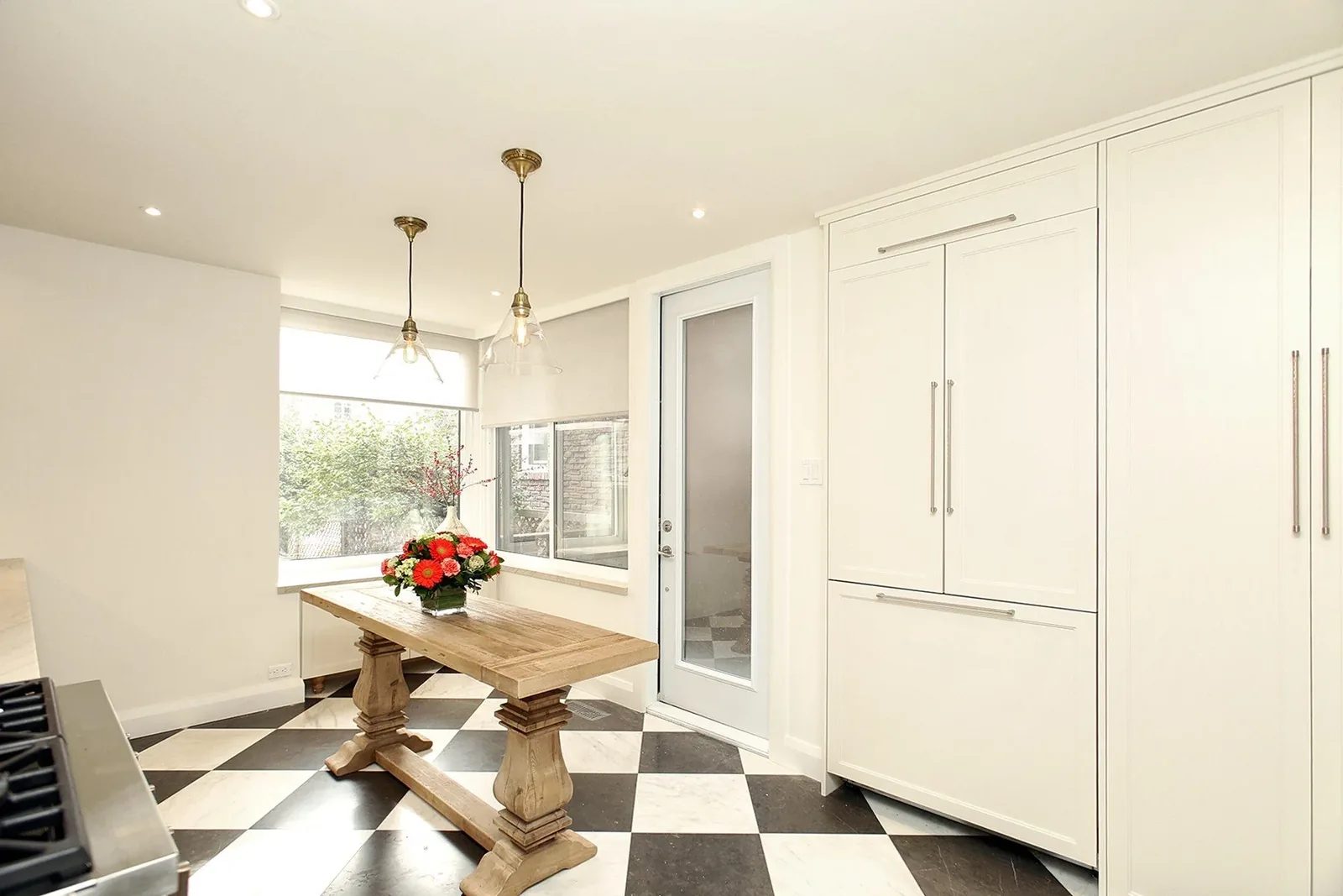 Bright kitchen breakfast nook with white cabinetry, checkerboard tile, oak table, and pendant lighting.