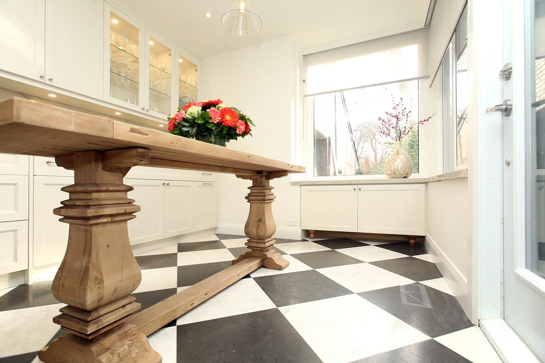 Renovated Toronto kitchen featuring white shaker cabinets, a large wooden dining table, and a black and white checkerboard.