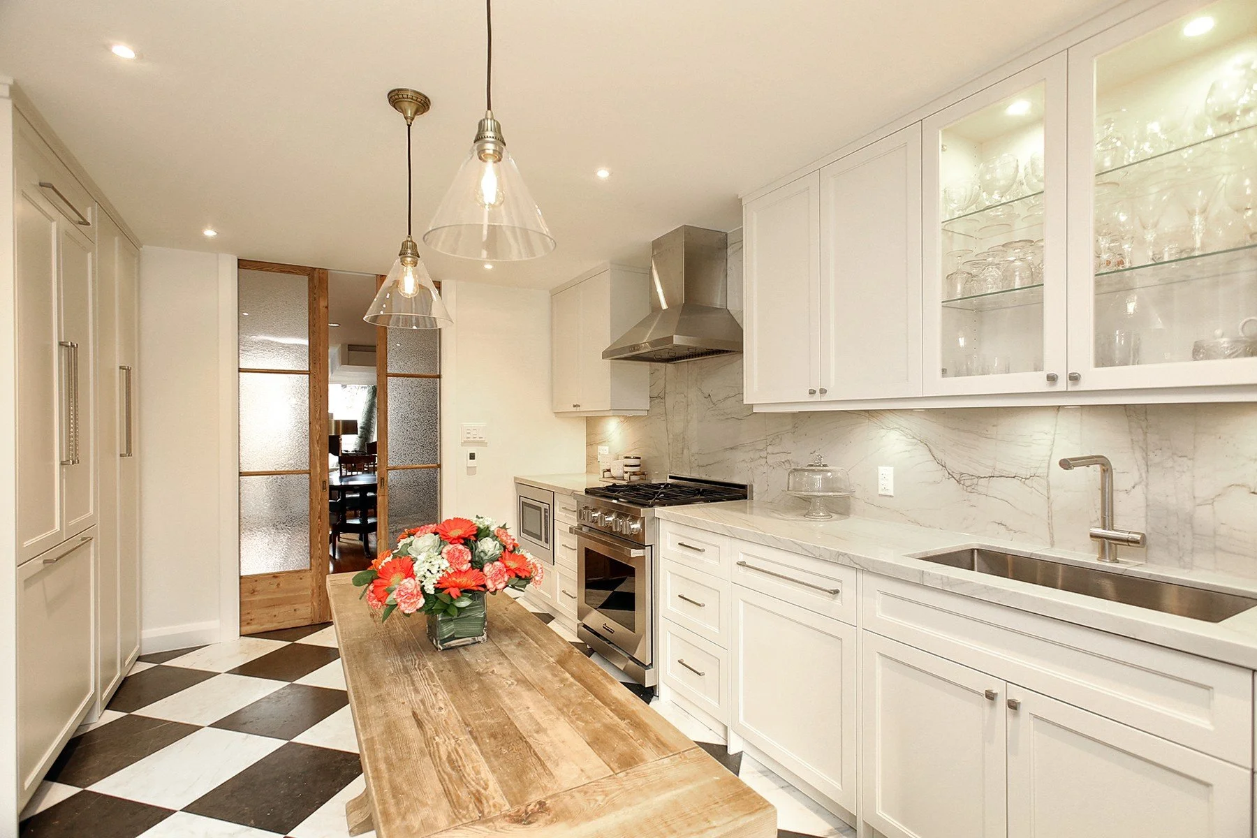 Bright renovated kitchen with white cabinetry, marble-look walls, oak island, and black and white floor tiles.