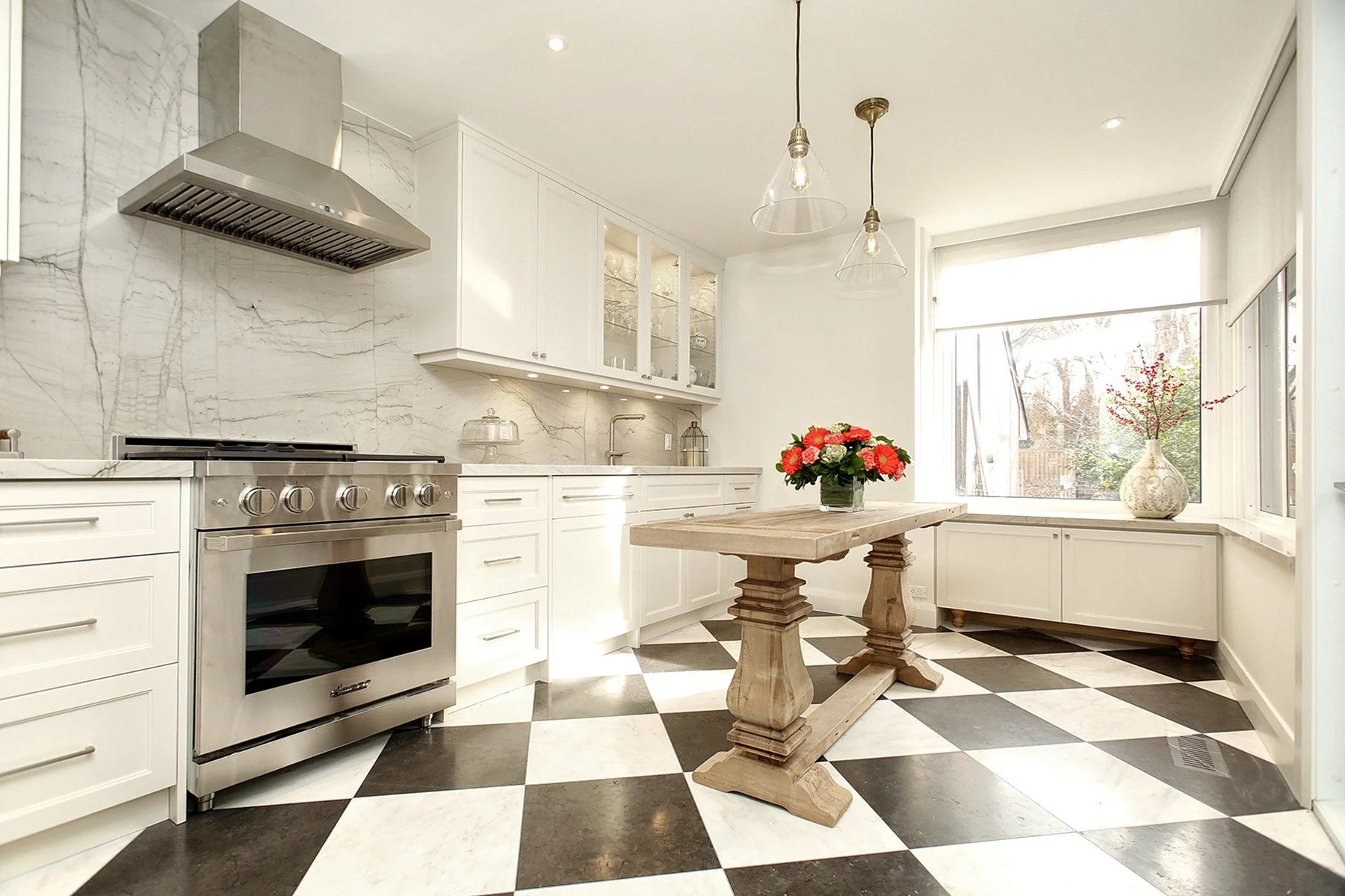 Bright white kitchen renovation with marble walls, checkered floor, wood island, and large window seating.