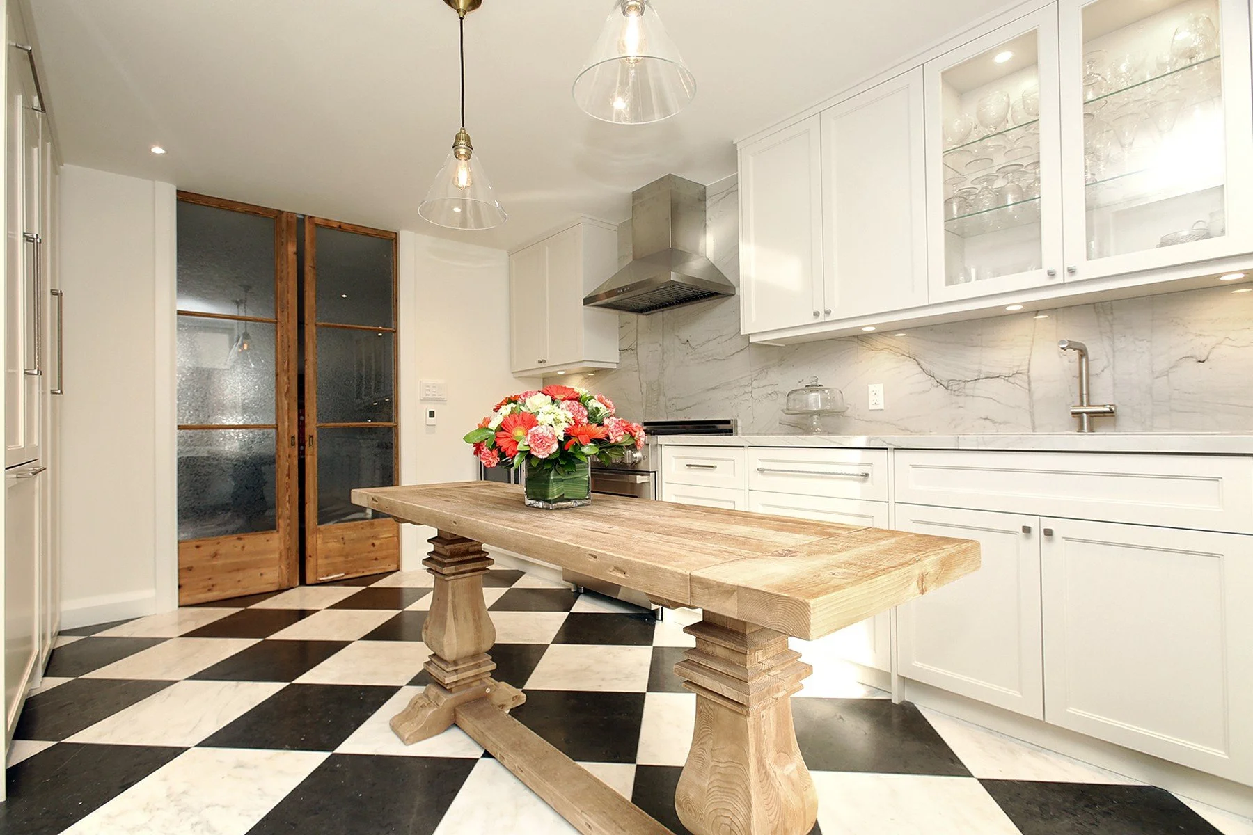 Bright renovated kitchen with white cabinetry, marble-look surfaces, chequered floor and a rustic oak table.