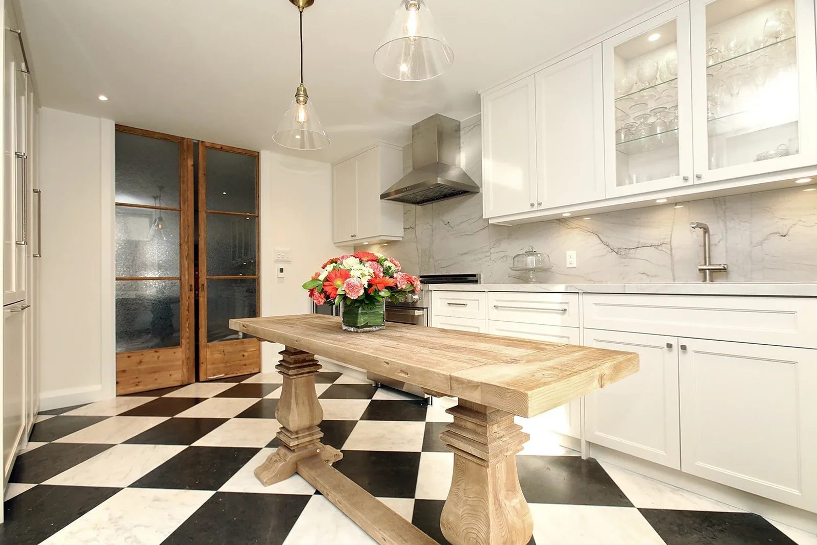 Bright renovated kitchen with white cabinetry, marble-look surfaces, chequered floor and a rustic oak table.