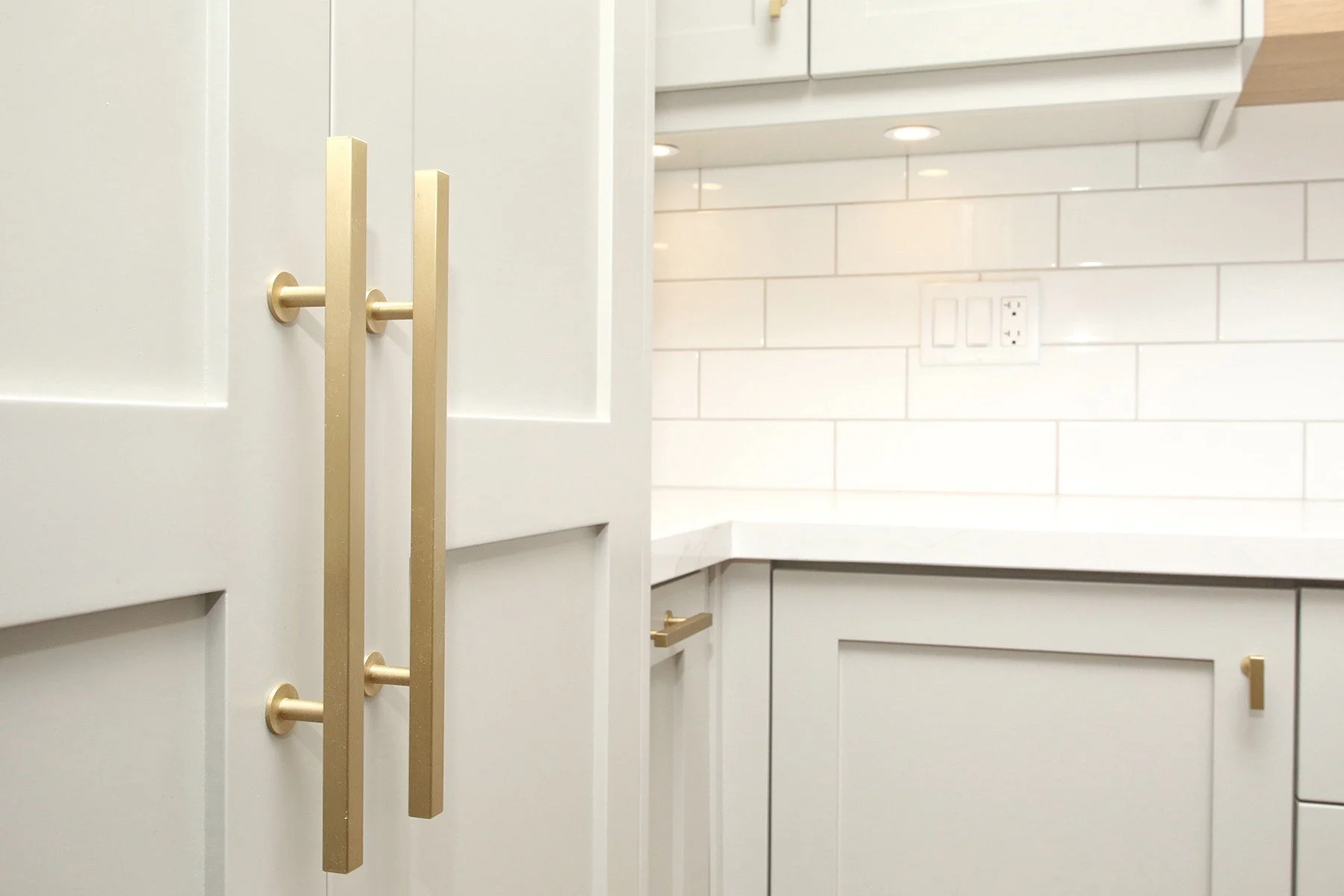 Warm white kitchen cabinetry with brushed brass pulls, quartz counters, and glossy subway tile.