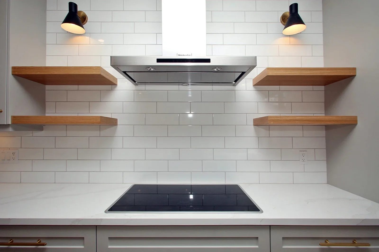Renovated Toronto kitchen with white subway tile, oak shelves, brass pulls and a sleek cooktop.