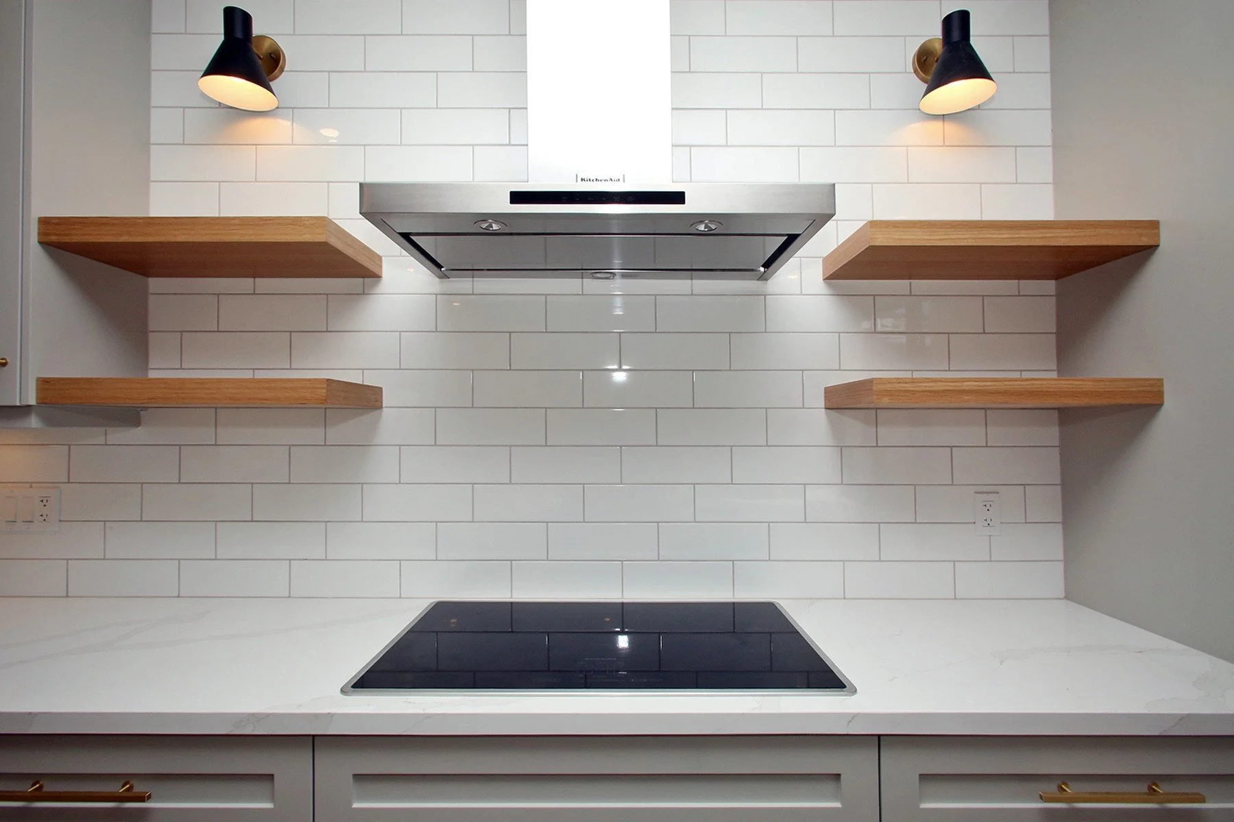 Renovated Toronto kitchen with white subway tile, oak shelves, brass pulls and a sleek cooktop.