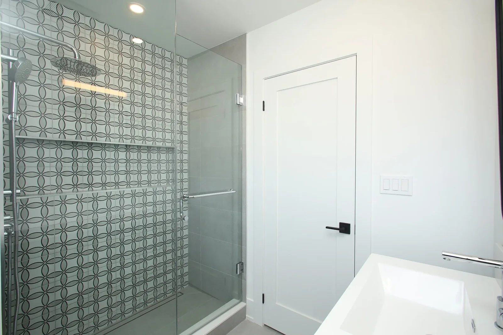 Finished bathroom with a glass shower, patterned tile wall, and bright white colour palette.