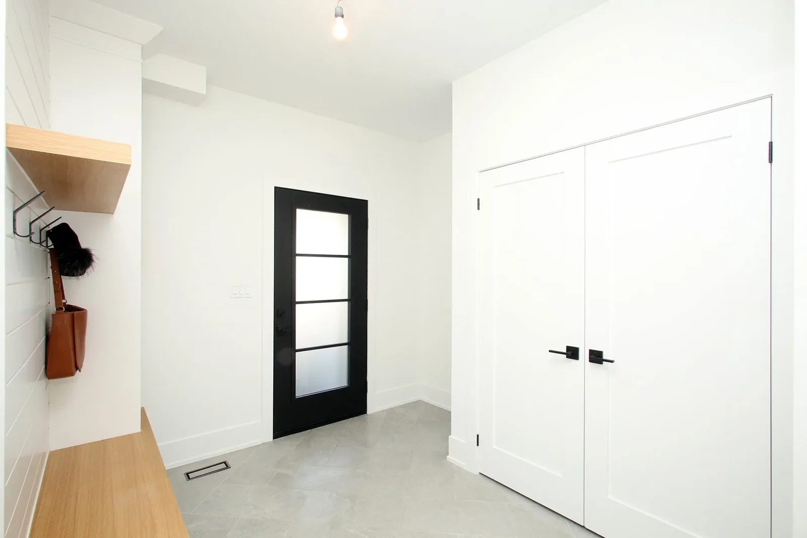 Bright renovated entry with grey tile, black door, white closet doors, and organised oak mudroom storage.