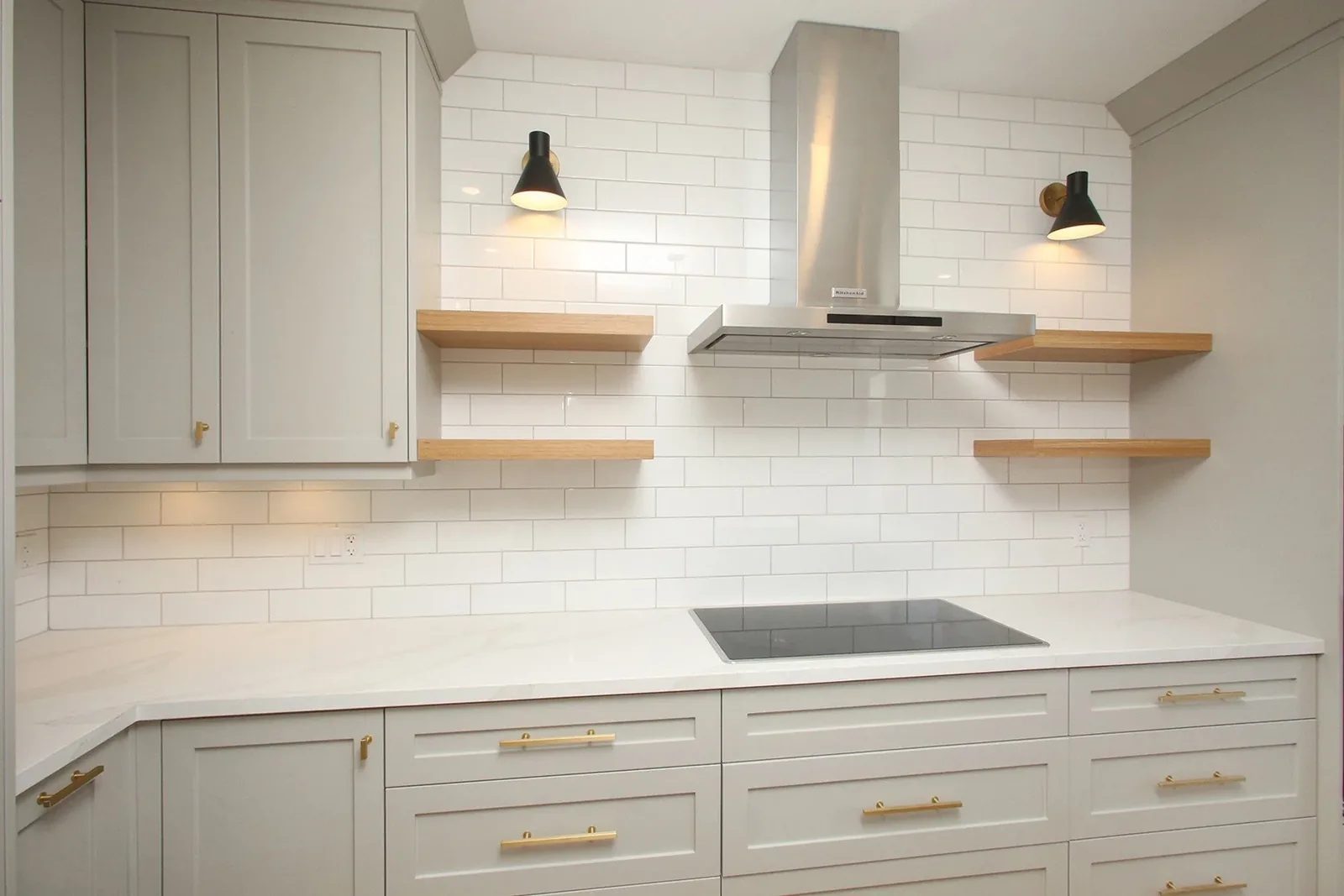 Finished Toronto kitchen with grey shaker cabinets, white tile, oak shelves, brass pulls, and a centre cooktop.