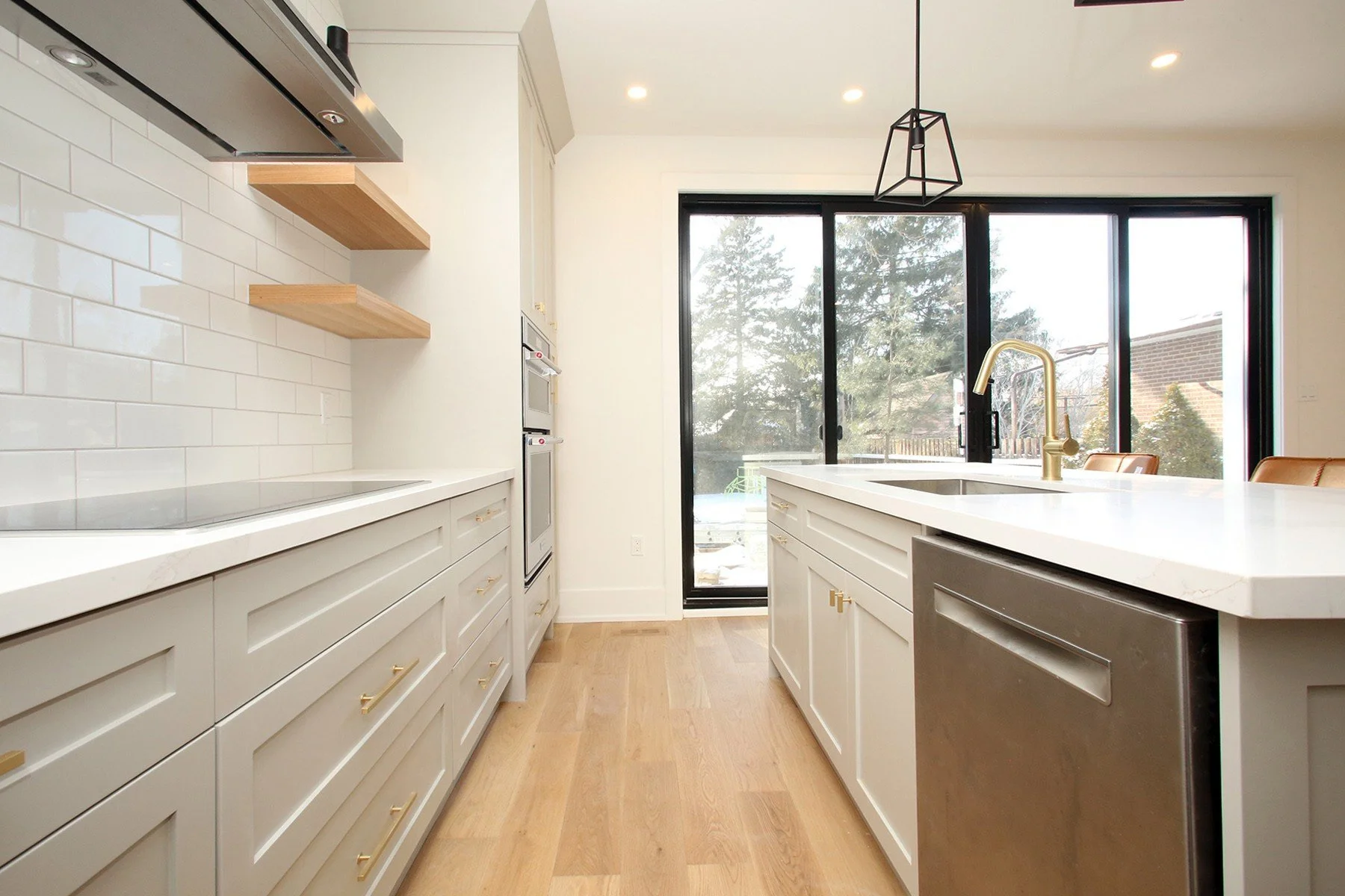 Bright Toronto kitchen with warm white shaker cabinets, oak floors, brass hardware and a large quartz island.