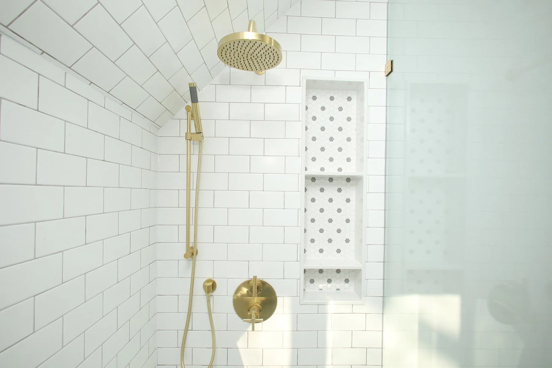 Bright white tiled shower with brushed brass fixtures, a glass panel, and a recessed niche.