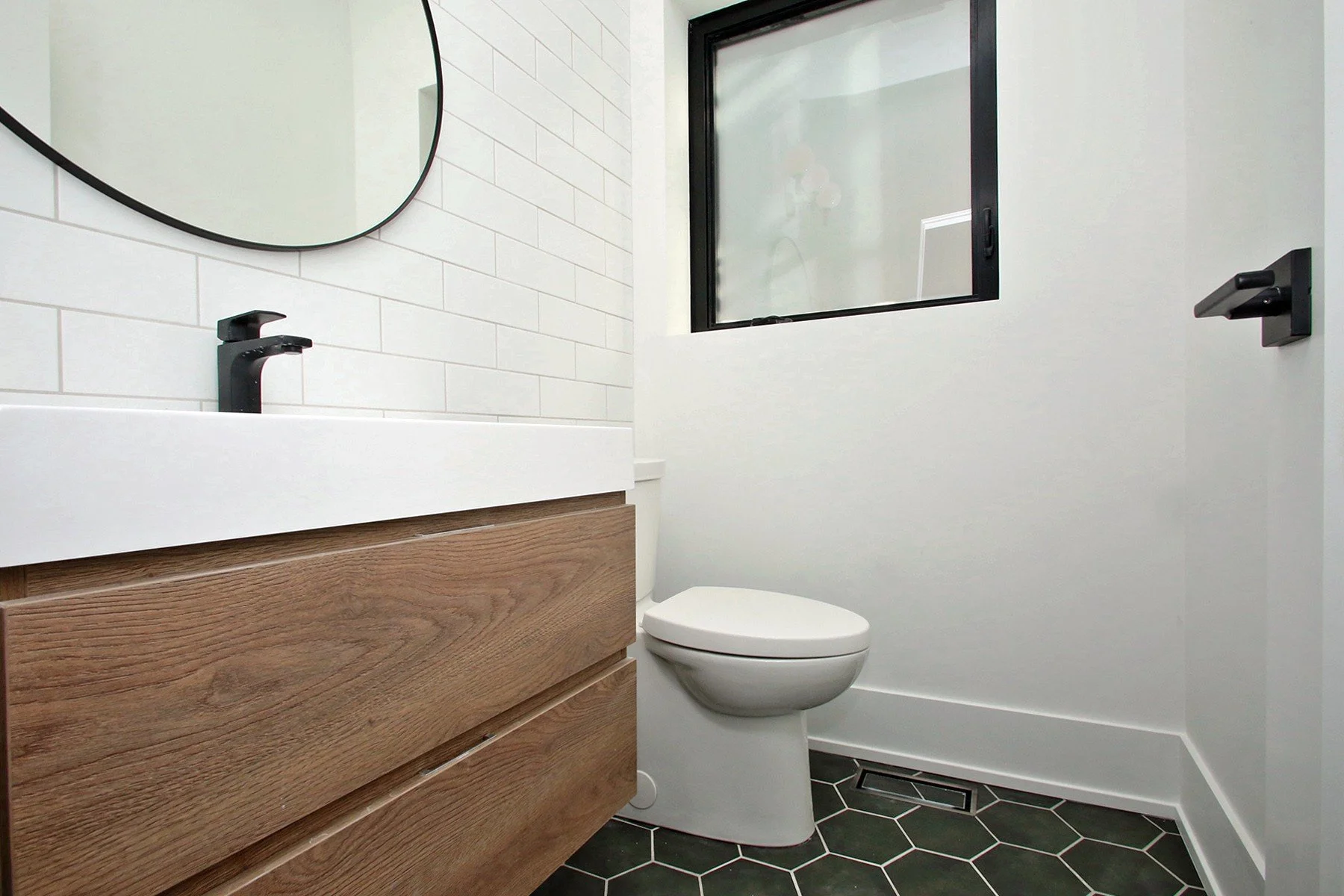 Finished bathroom with oak vanity, black fixtures, white tile, and dark hex floor for a Toronto renovation.