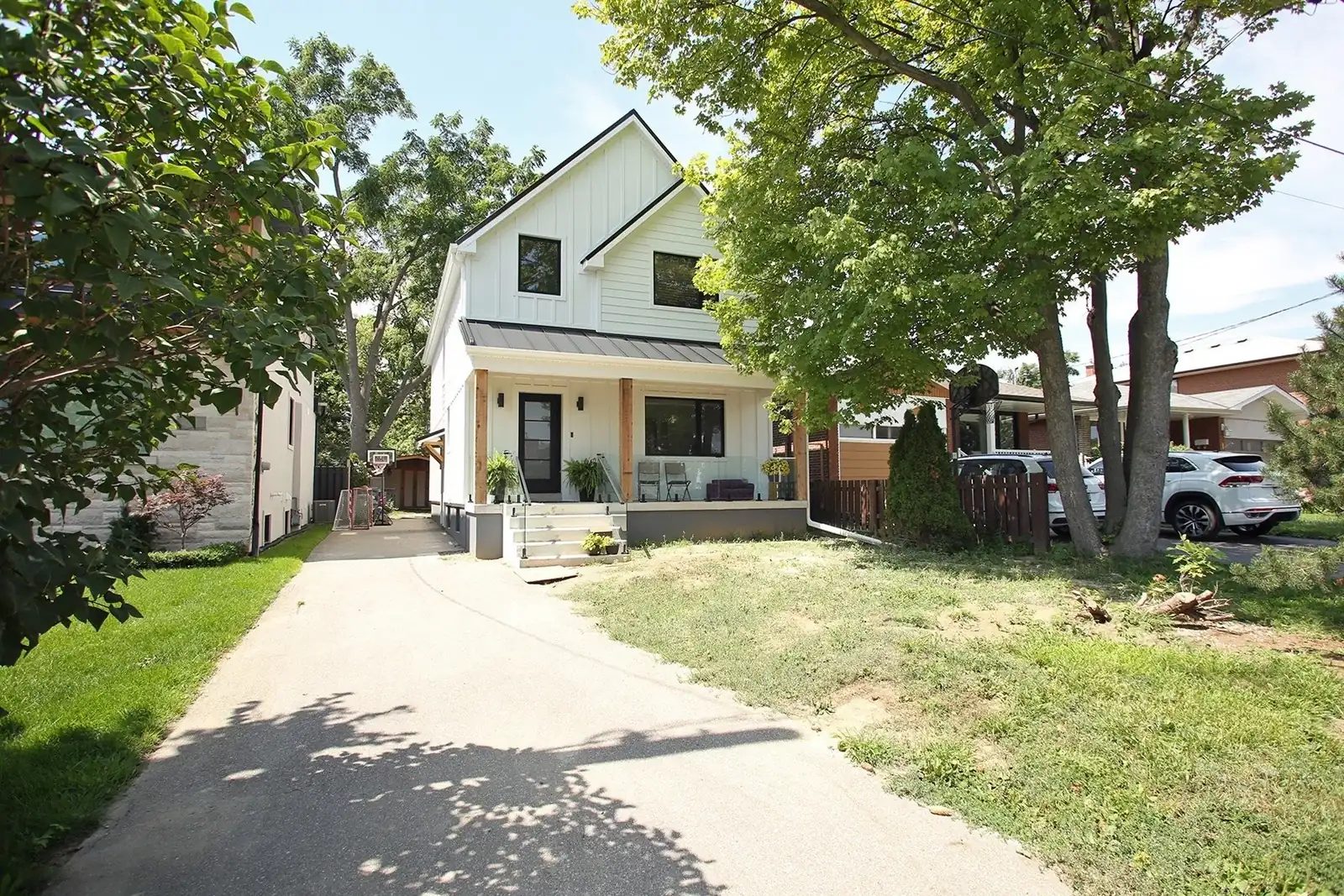 White two-storey Toronto home with black windows, a covered porch, and a concrete driveway.