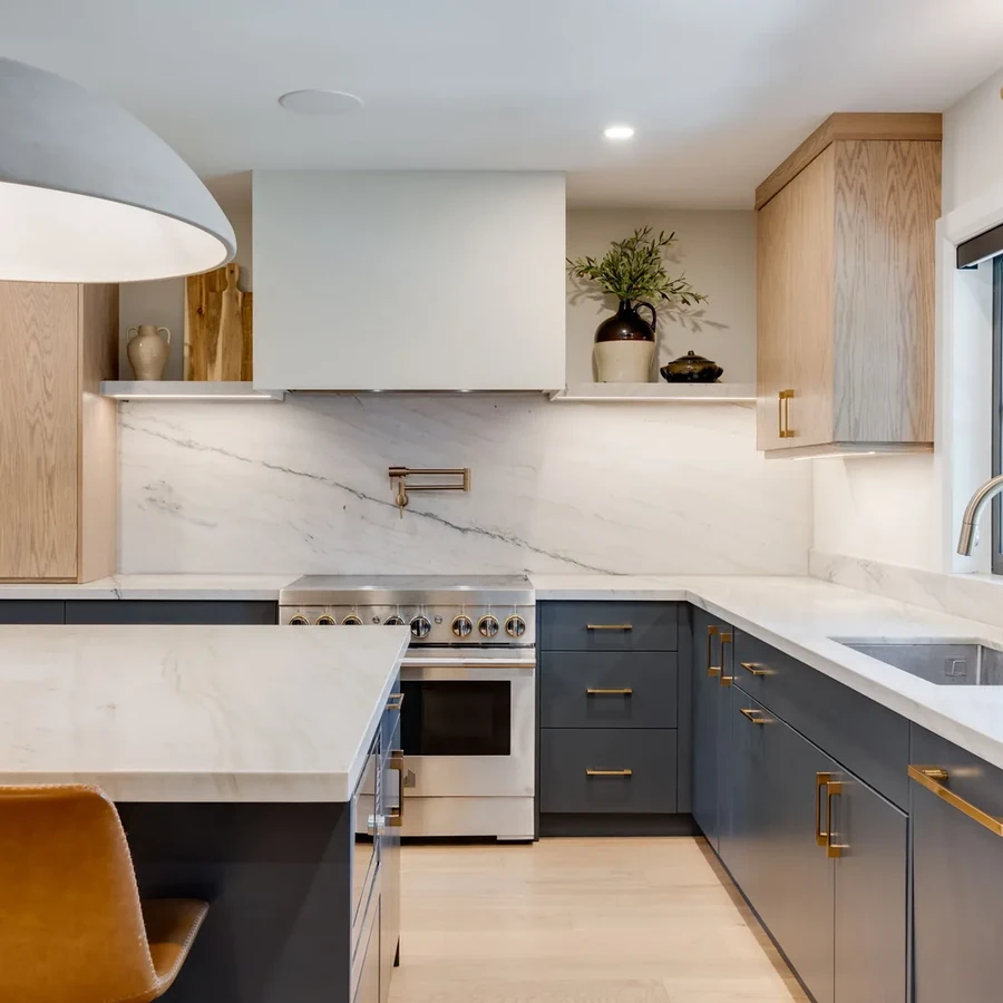 Peace Restored: a marble waterfall island with an amber leather stool and brass faucet, set against navy and white oak cabinetry, by Waterfront Home Improvements