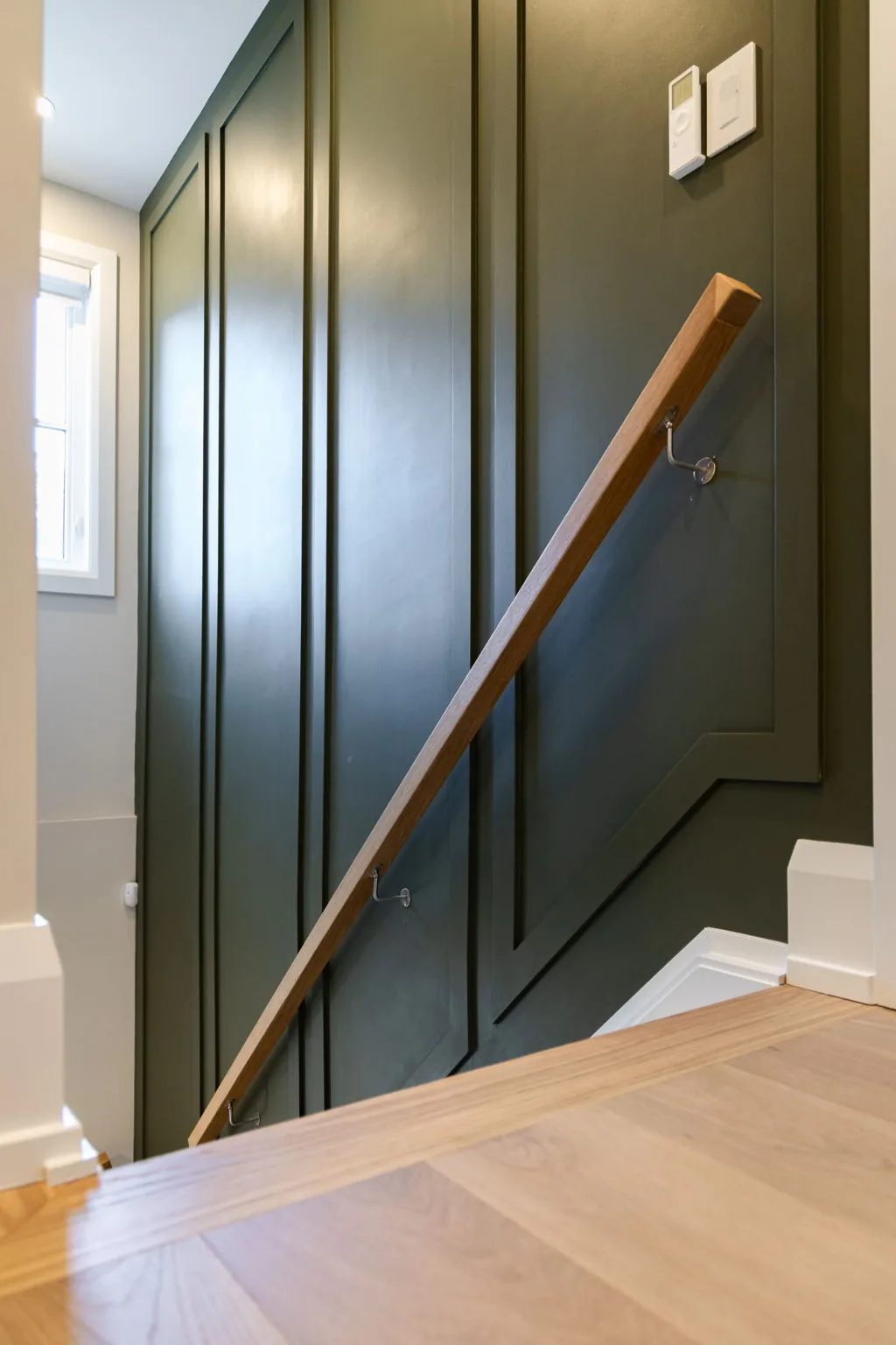 Staircase with deep green panelled walls, a natural oak handrail, and crisp white risers.