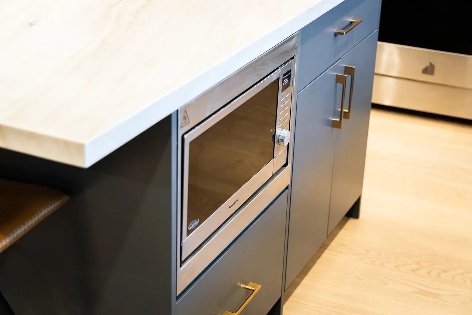 Island end with a mitred stone edge, an integrated microwave drawer and a brass bar pull on the navy cabinetry.