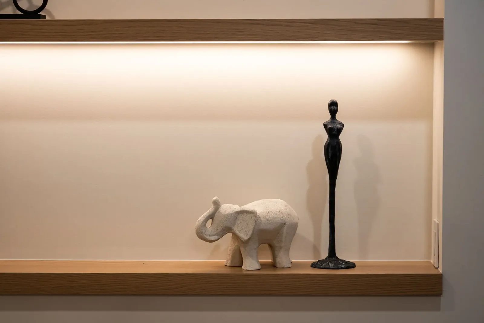 Lit white oak display shelves in the dining room niche, holding a carved stone elephant and a slender black figurine.