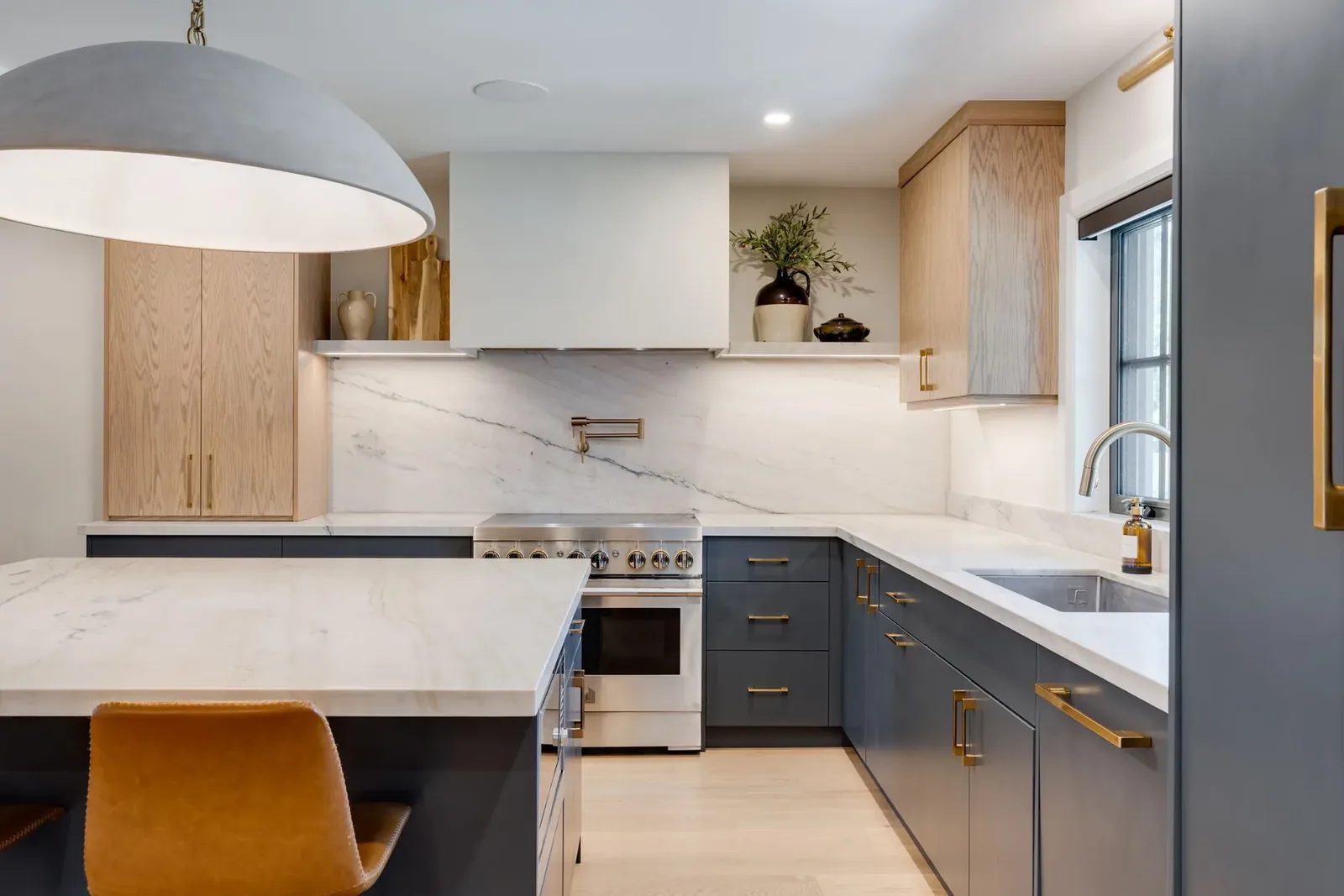 Wide view across the quartzite waterfall island to the navy base cabinetry, the white oak uppers and the stone slab backsplash beyond.