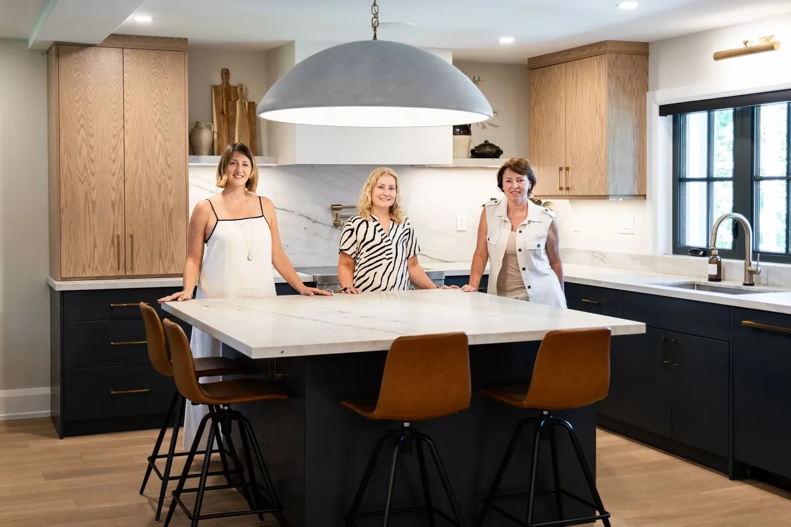 Three people standing together at the quartzite island beneath the dome pendant, with the white oak and navy kitchen cabinetry behind them.