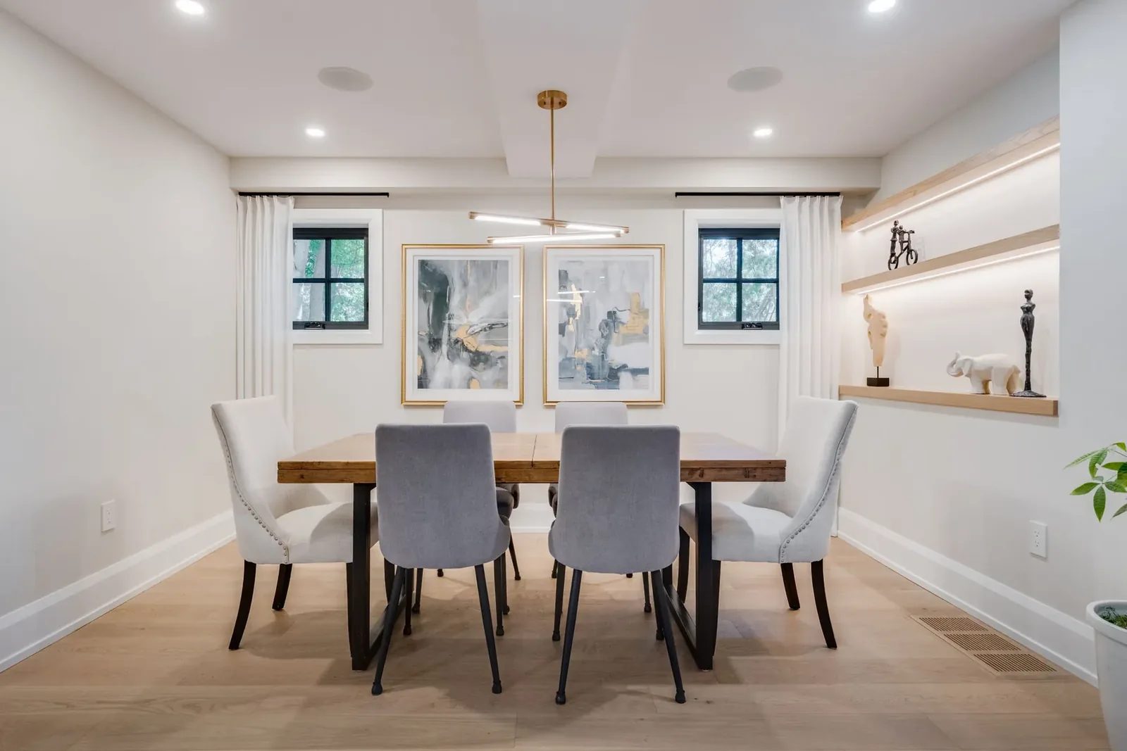 Dining room straight on, with a wood table between two black casement windows, a linear pendant and a lit oak display niche on the side wall.