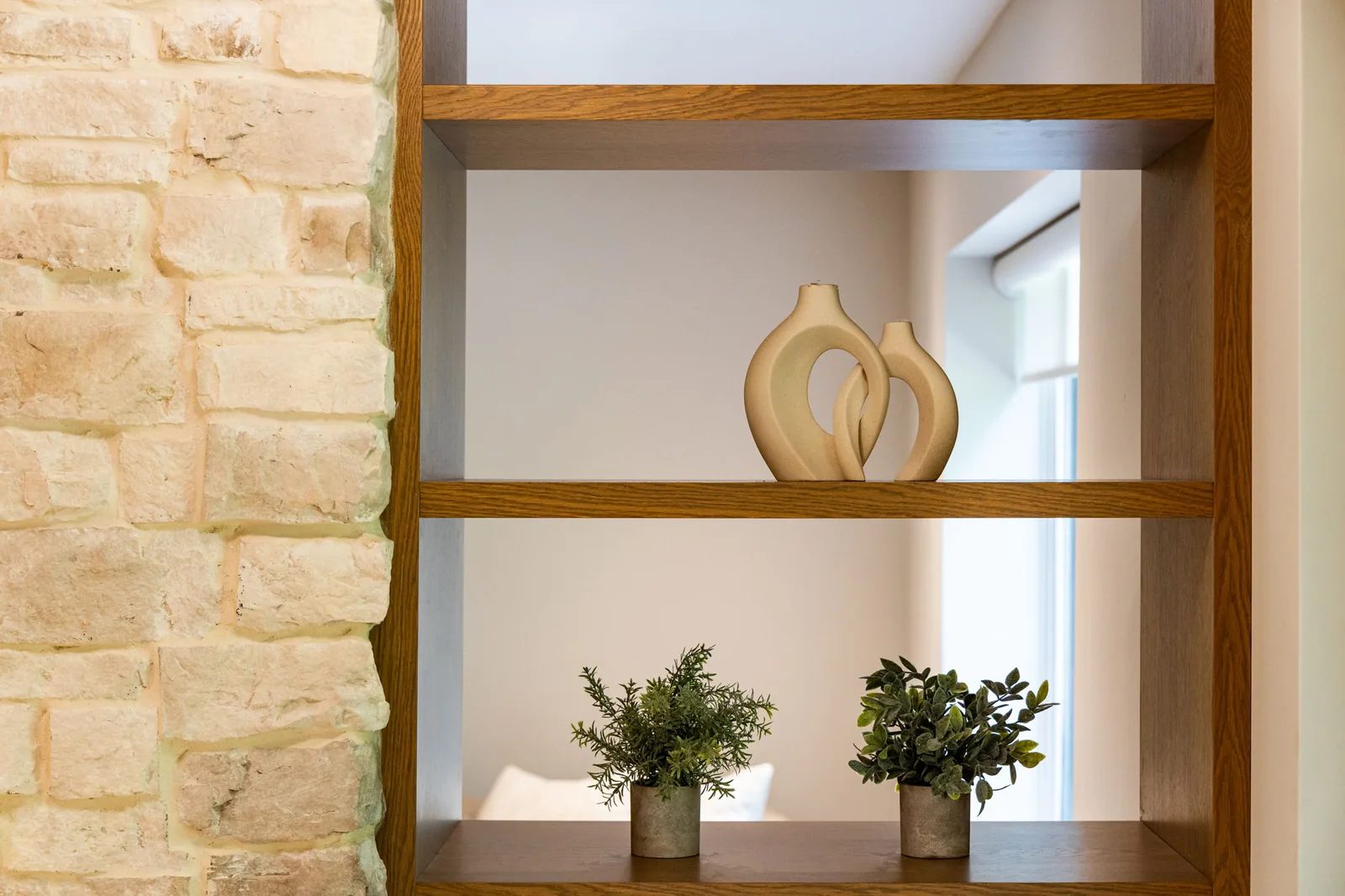 Natural stone feature wall with floating white oak shelves styled with sculptures and greenery.