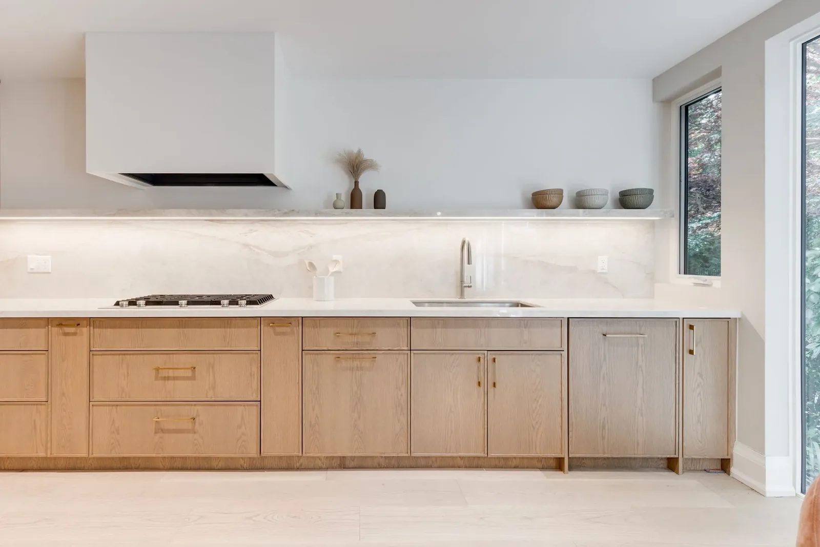 Kitchen elevation with a gas cooktop and sink set into the stone counter, beneath a lit full-length stone shelf and marble slab backsplash.