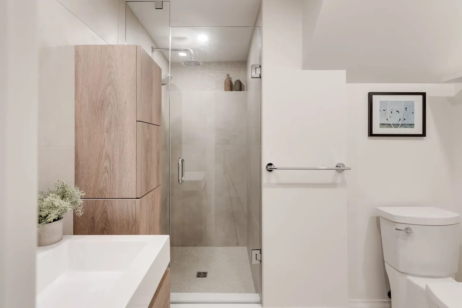 Walk-in shower behind frameless glass with a round rainfall head and a penny-mosaic accent band, beside a wood-grain storage tower.