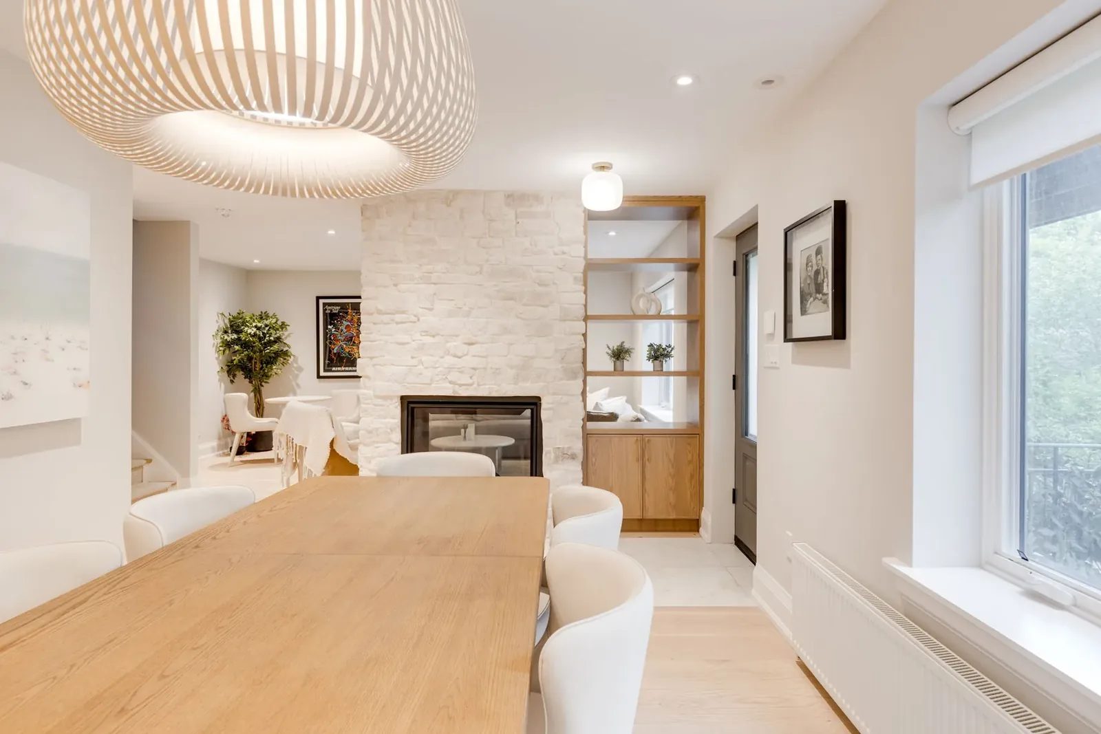 Dining room looking past the whitewashed stone fireplace and oak shelf niche to a sitting corner beyond, with a grey glass-panelled door at the entry.
