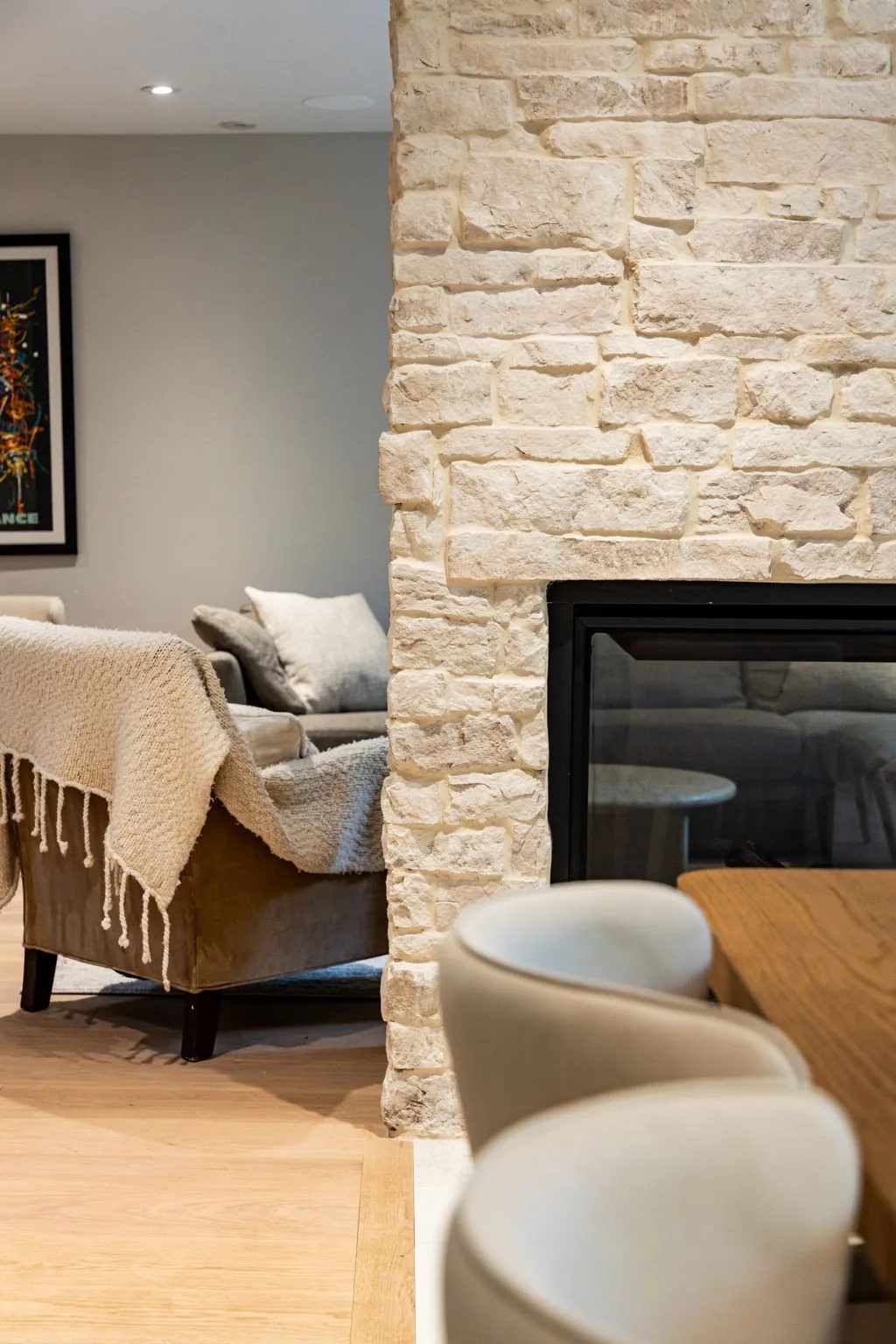 Whitewashed stone fireplace column seen from the dining side, a knitted throw over the olive velvet armchair and the linen sofa beyond.