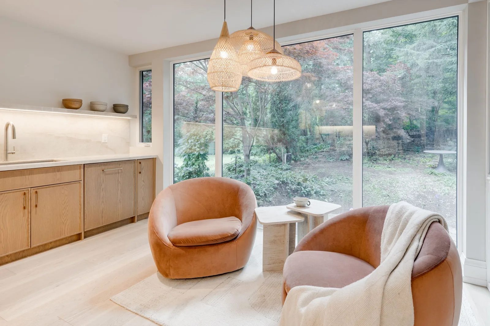 Sitting area with orange leather swivel chairs and a marble-topped coffee counter beneath cluster pendants, facing a wall of windows onto the wooded ravine.