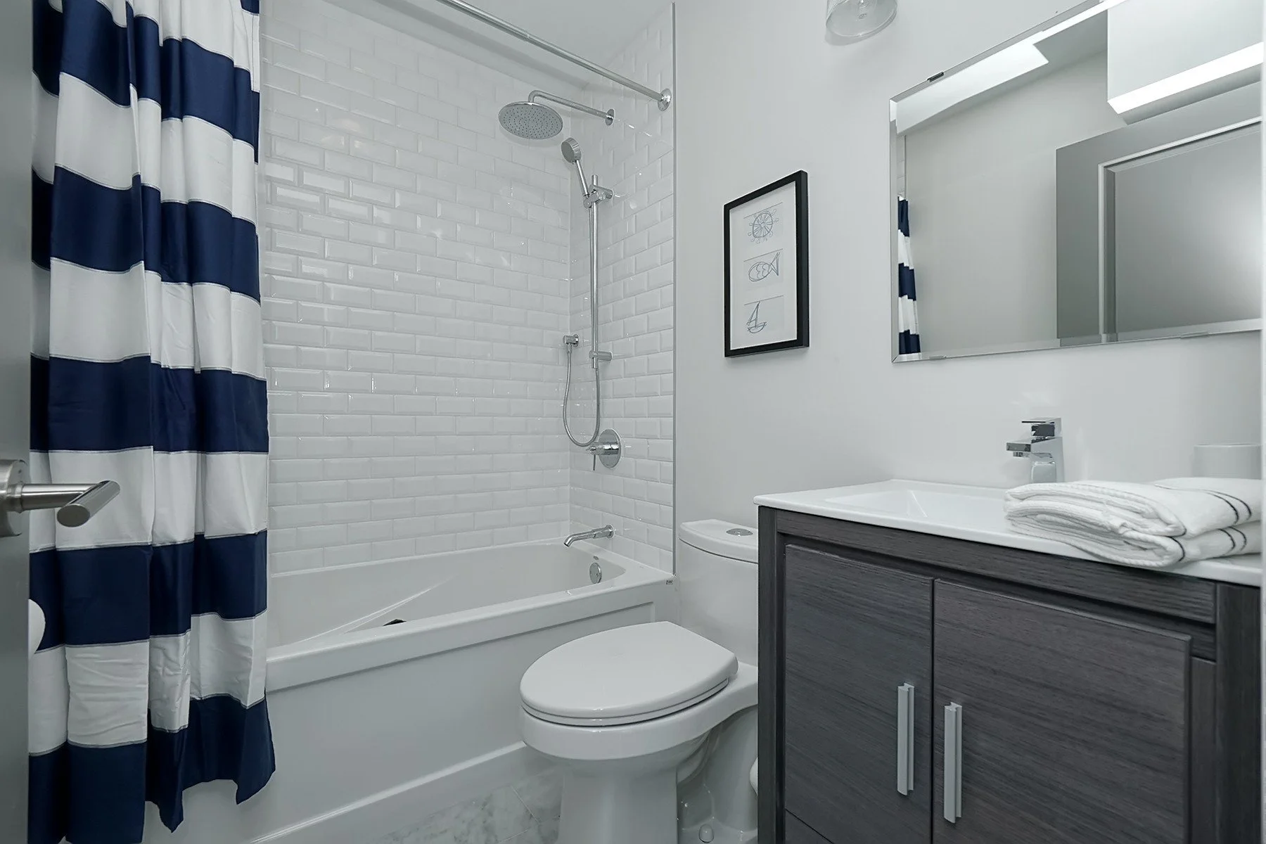 Compact bathroom with white subway tile, navy striped curtain, chrome fixtures and a charcoal vanity.