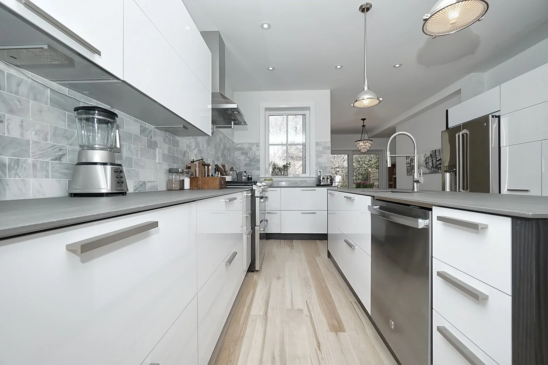 Bright white Toronto kitchen renovation with grey tile backsplash, island, pendants and light oak flooring.
