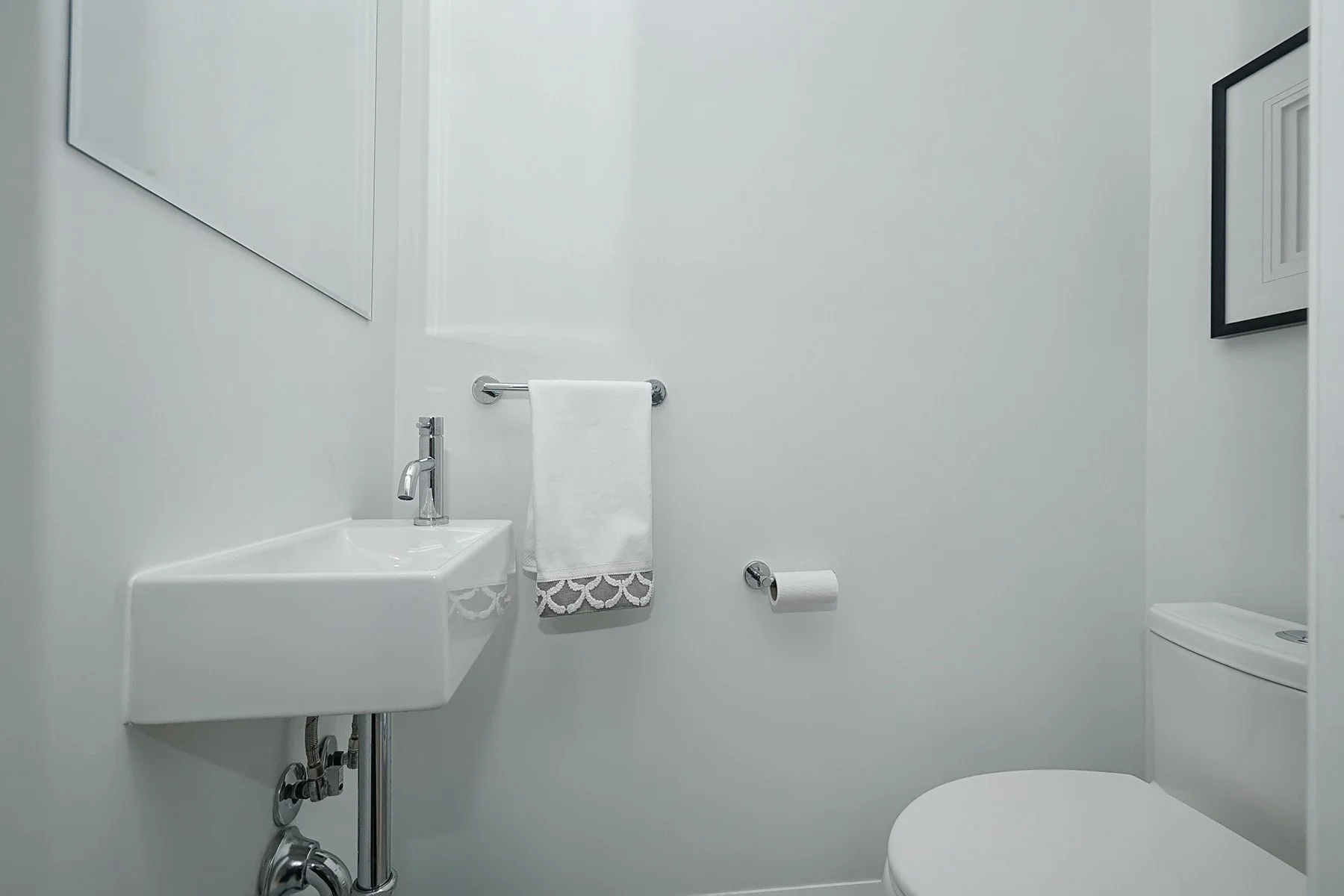 Compact white powder room with a wall mounted sink, chrome fixtures, towel bar, and toilet.