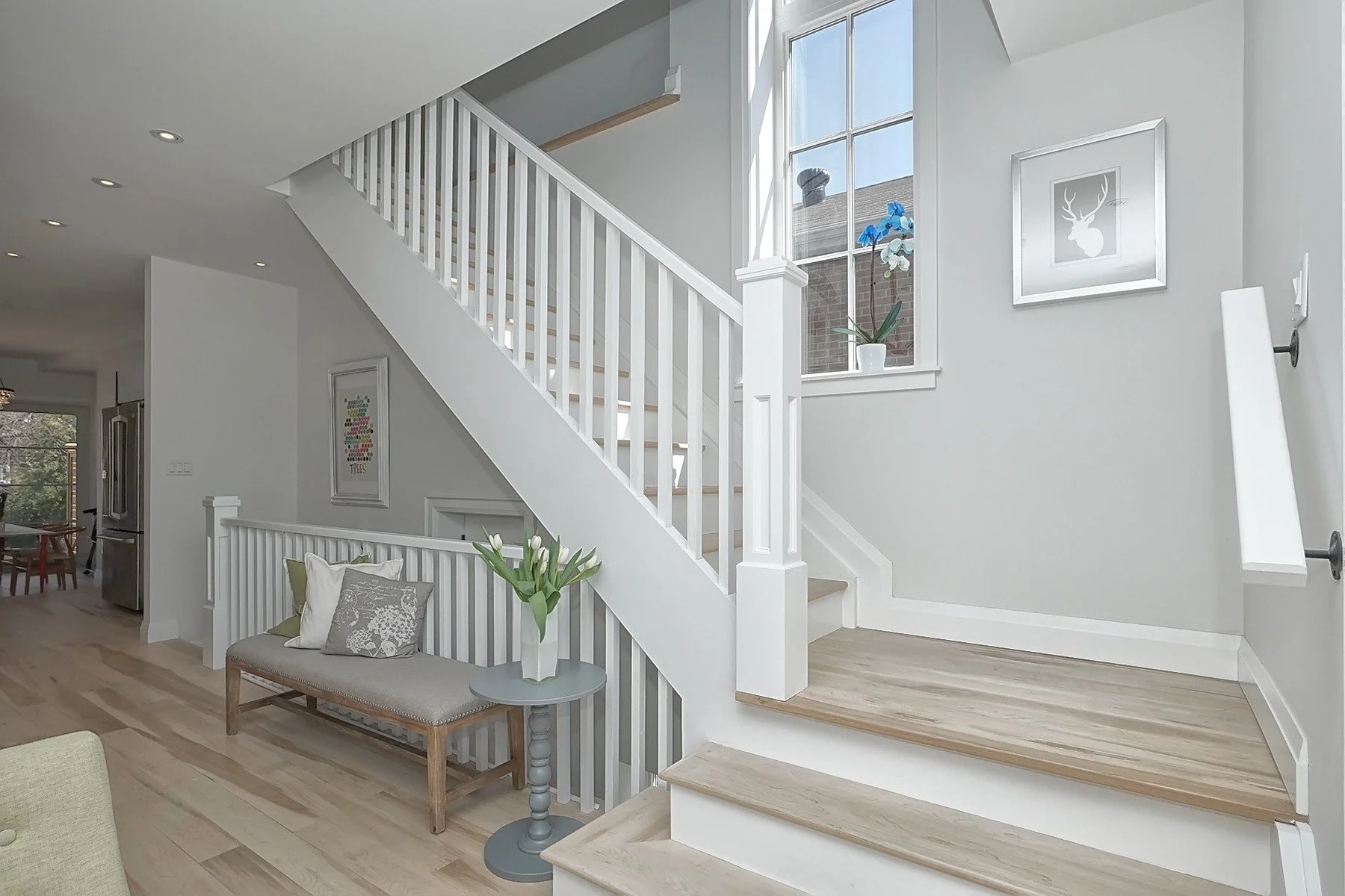 Bright renovated entry with white staircase, pale grey walls, and natural wood flooring.