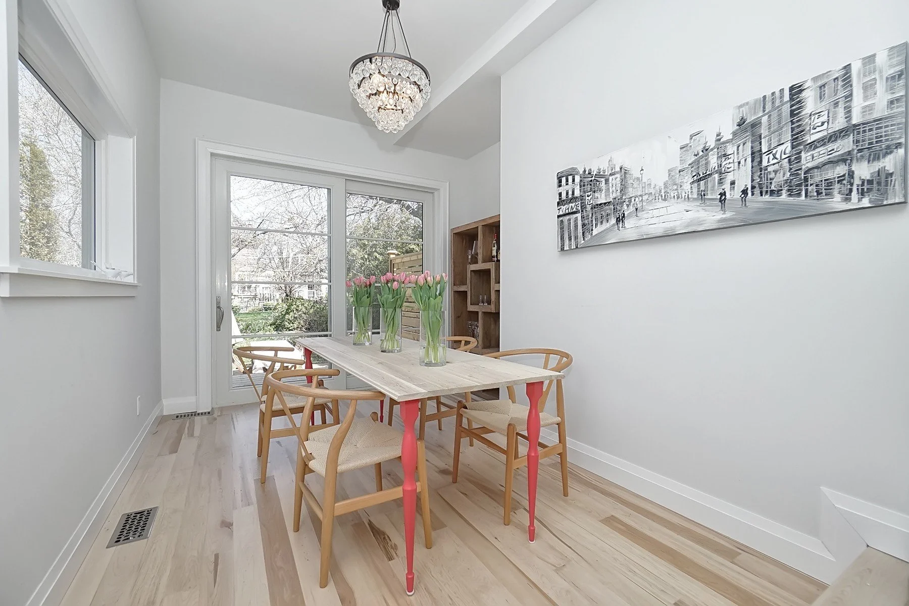 Bright Toronto dining room with warm white walls, pale hardwood flooring, large windows, and a crystal chandelier.
