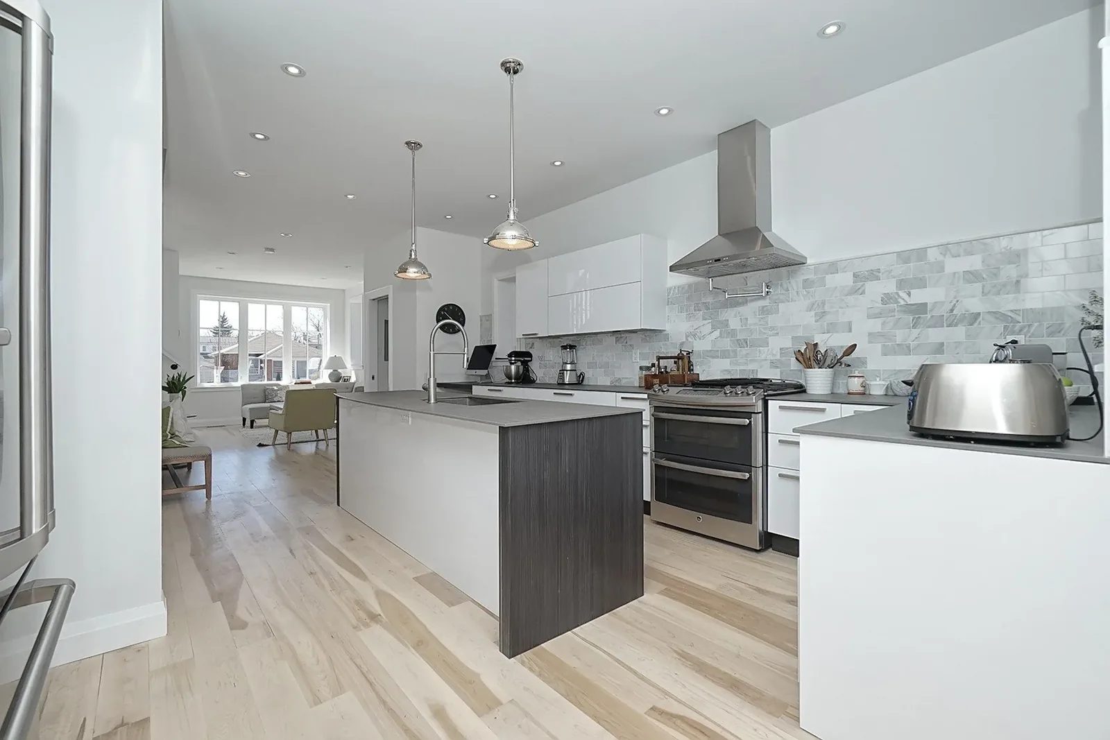 Renovated open-concept kitchen with white cabinetry, a grey island, marble subway backsplash, and stainless appliances in the Sophisticated Coastal home.
