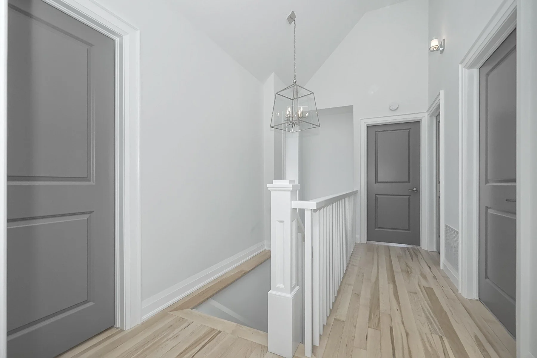 Finished upstairs hallway with grey doors, white trim, light wood flooring, and a glass pendant over the stairs.